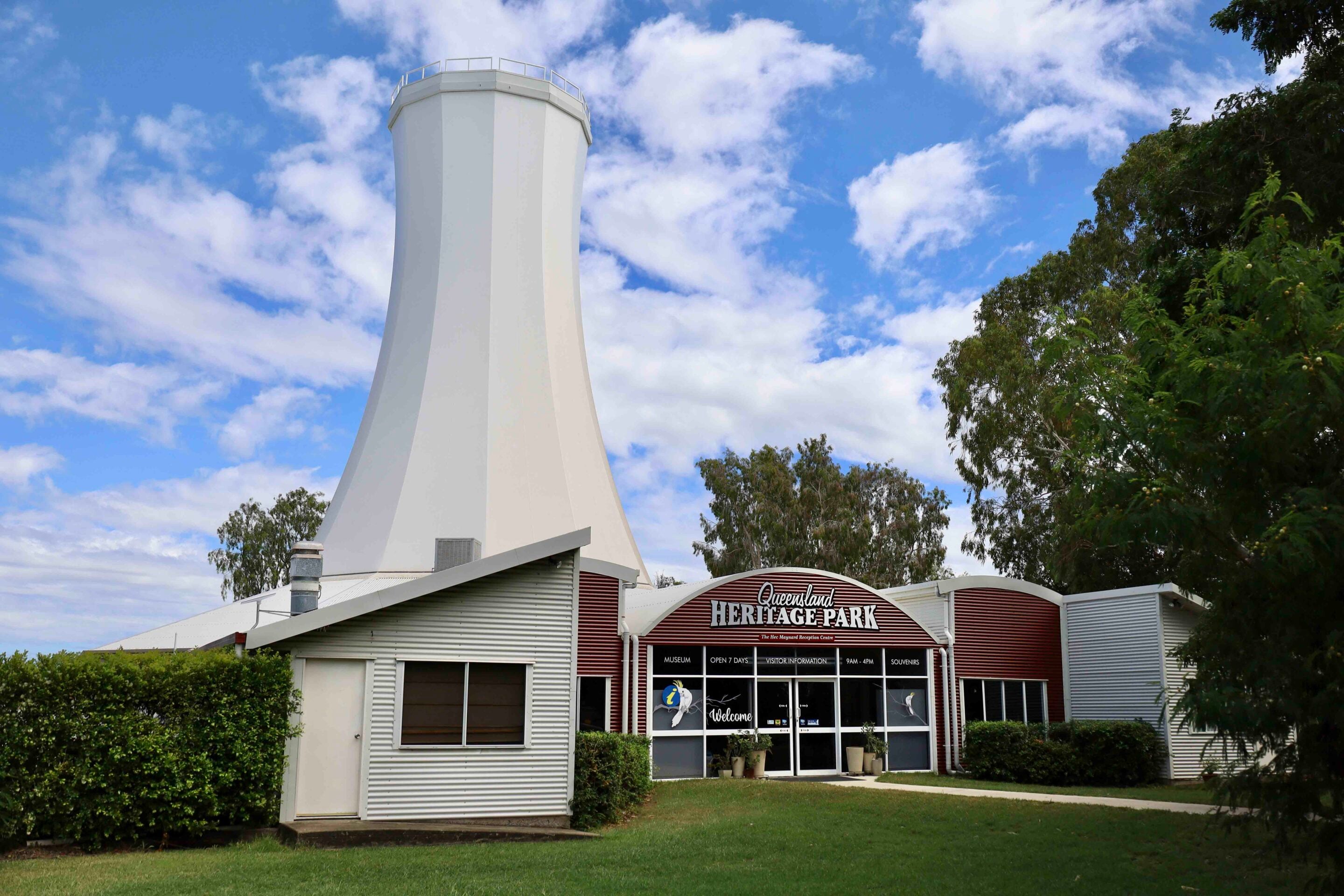 White observation tower rises beside the Queensland Heritage Park visitor center, under a blue sky with scattered clouds.