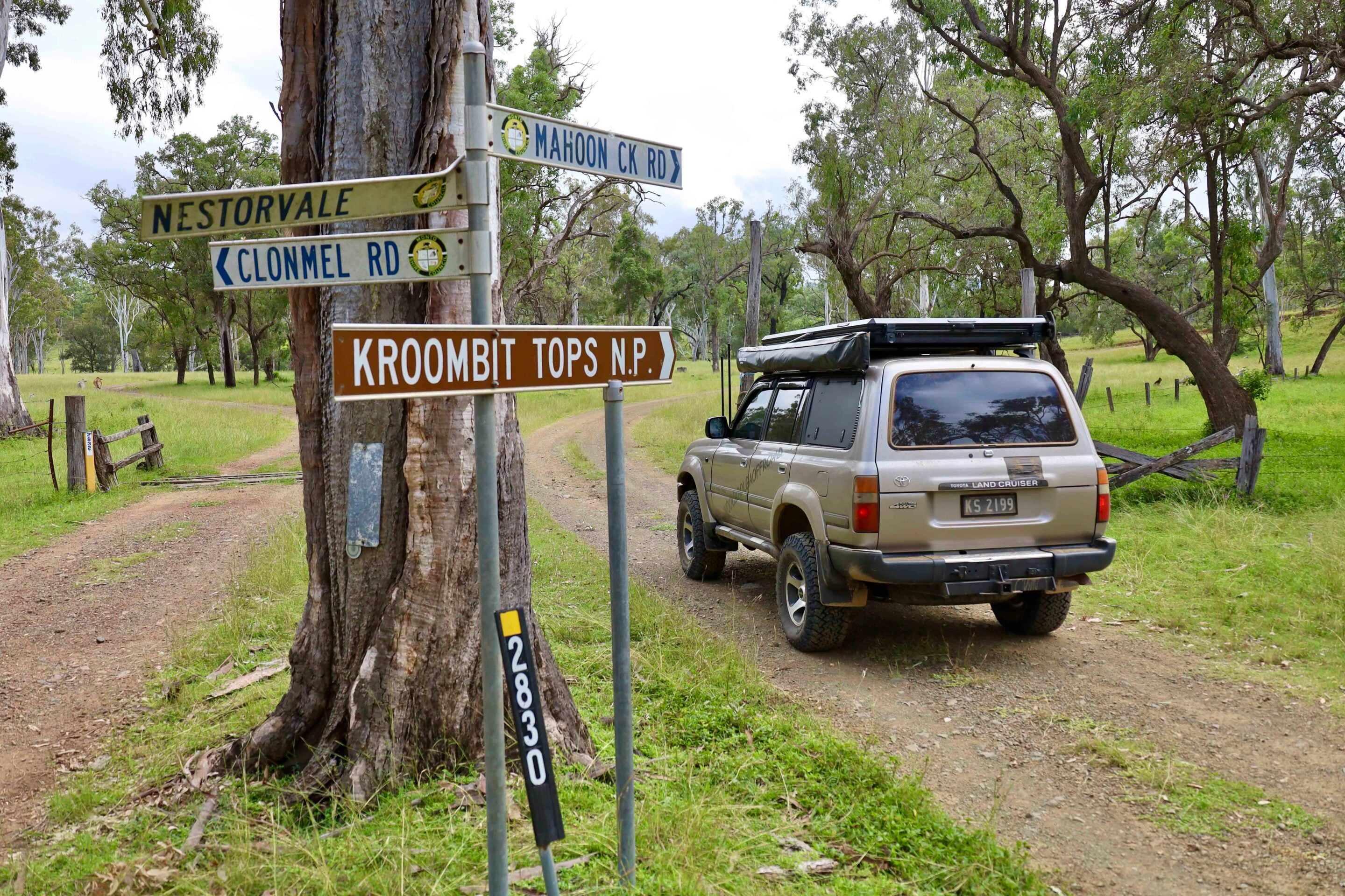 Off-road SUV parked at a rural intersection with signposts showing Nestorvale, Clonmel Rd, Mahoon CK Rd, and Kroombit Tops NP among trees.