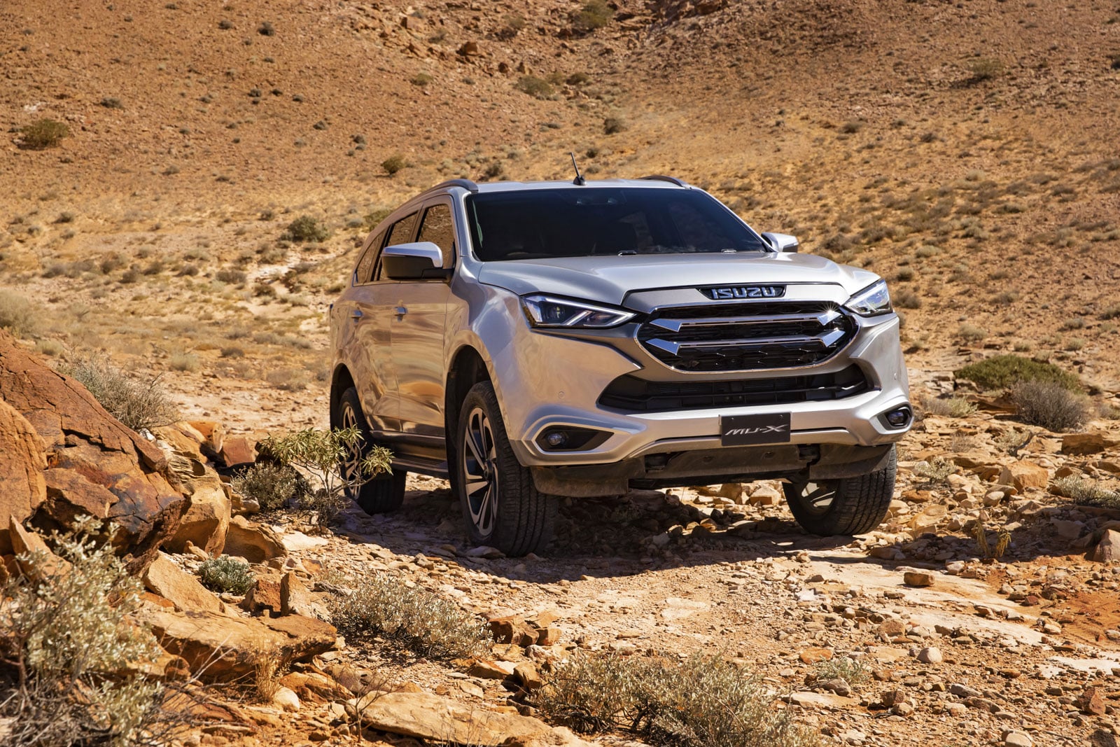 Silver Isuzu MU-X SUV parked on rocky desert terrain with arid hills in the background