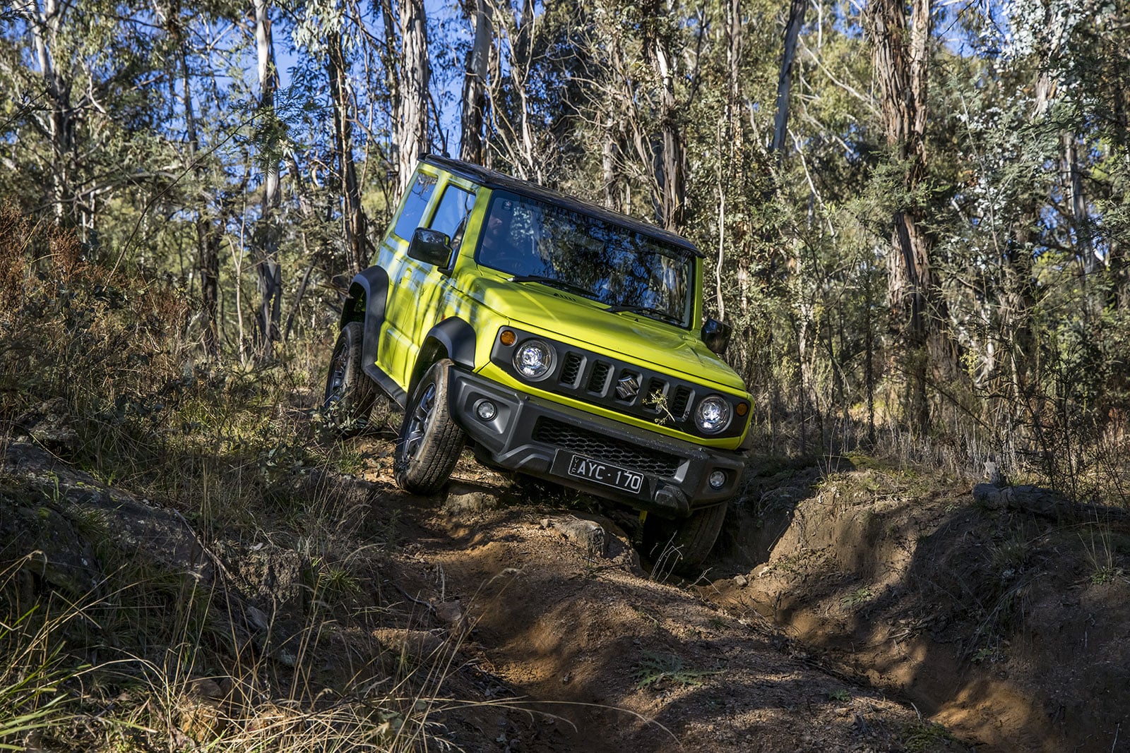 Green off-road SUV navigating a rocky dirt trail in a forest, tilting on uneven ground