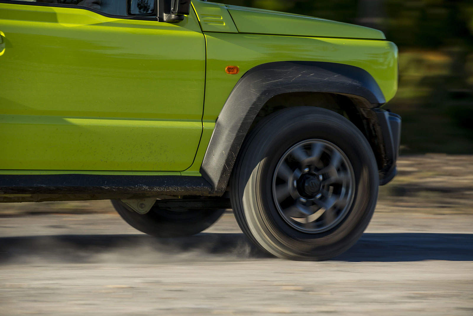 Lime-green off-road vehicle driving fast, wheel blurred and dust trailing on a road edge.