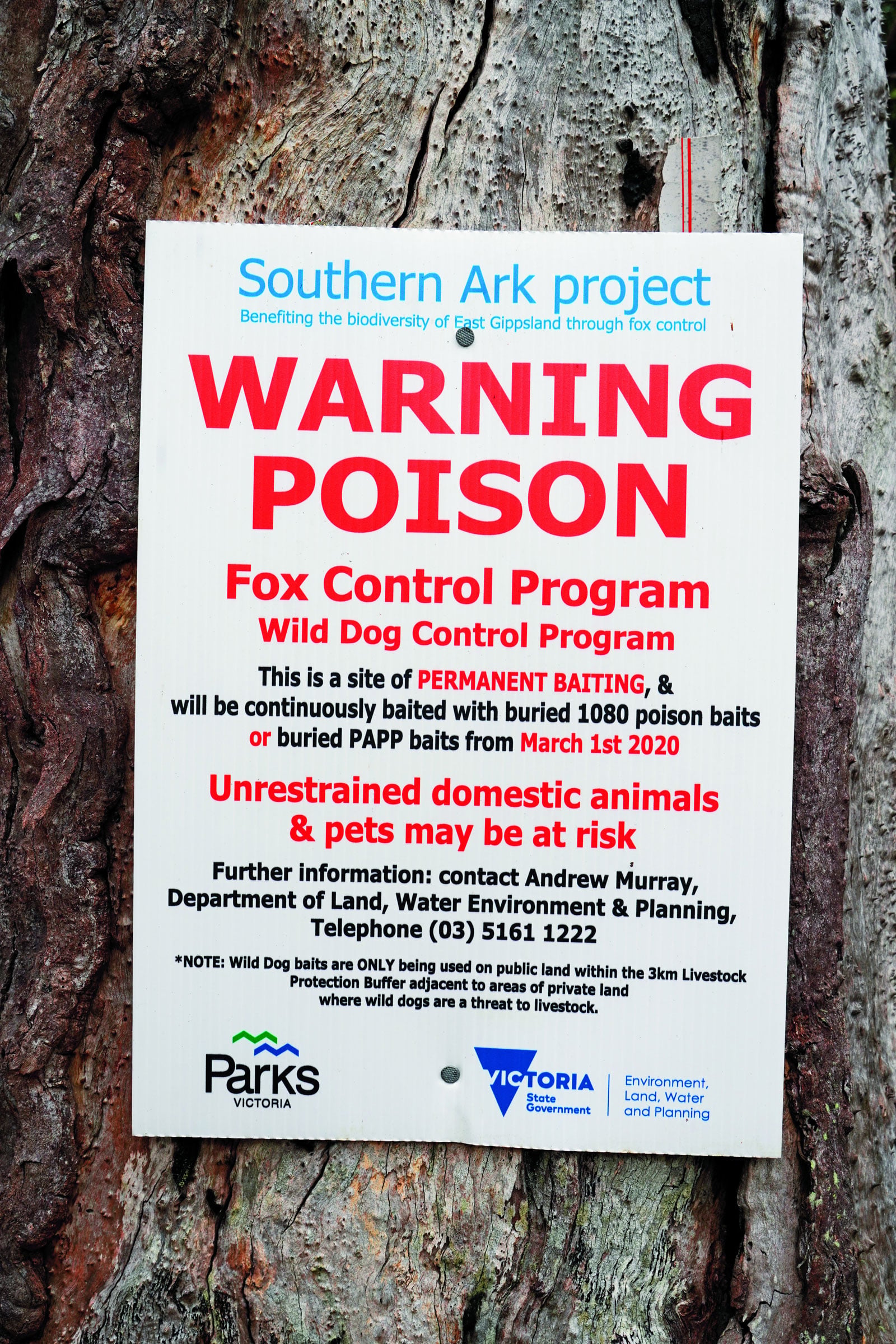 Sign on a textured tree condemns poison: large red 'WARNING POISON' with blue header text about a wildlife program nearby.