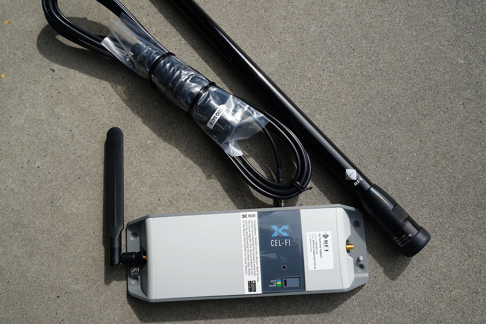 Cellular booster device labeled CEL-FI with attached antennas and cables on concrete surface.