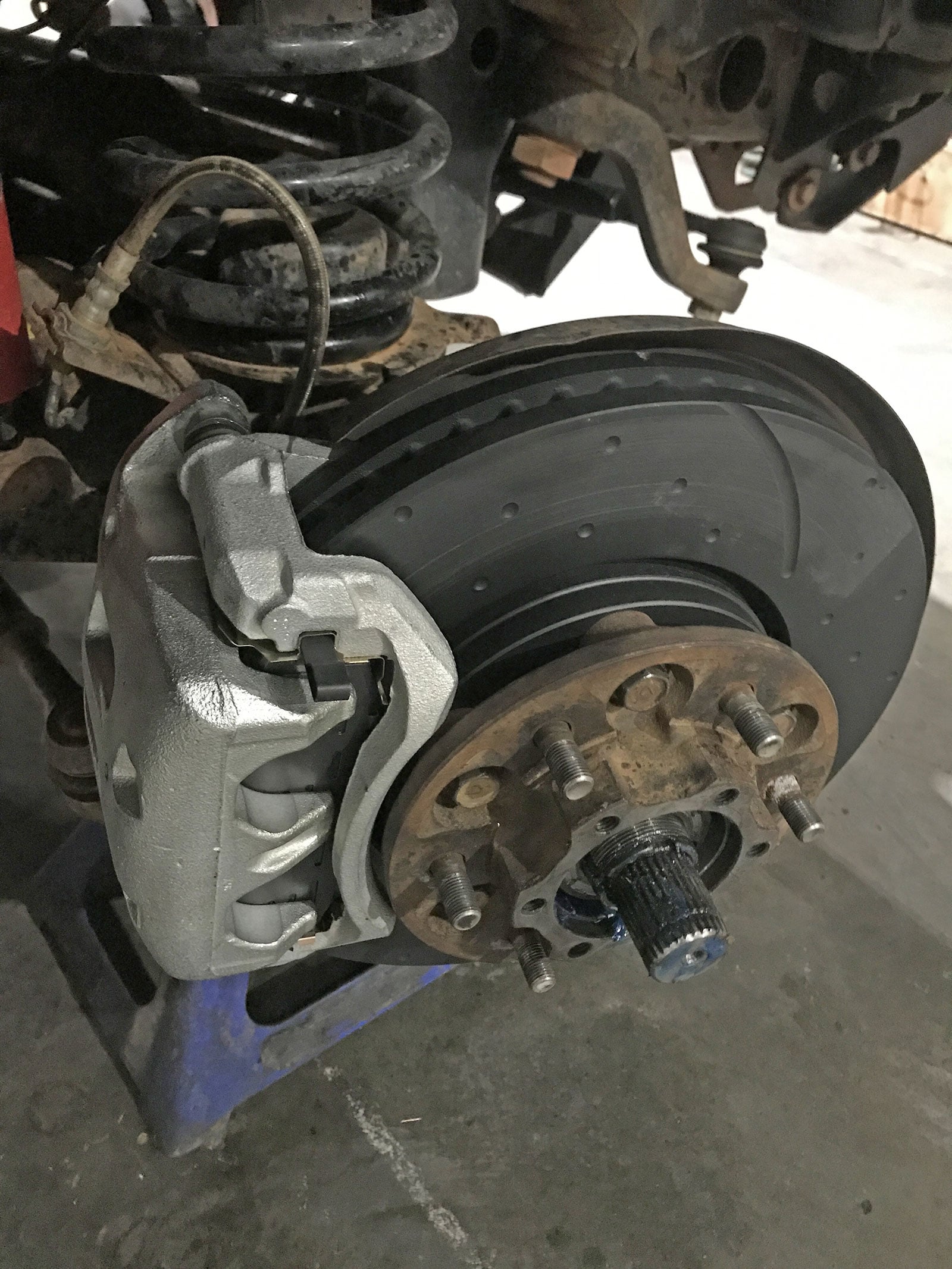 Front suspension and brake assembly with coil spring, caliper, and perforated rotor/hub visible