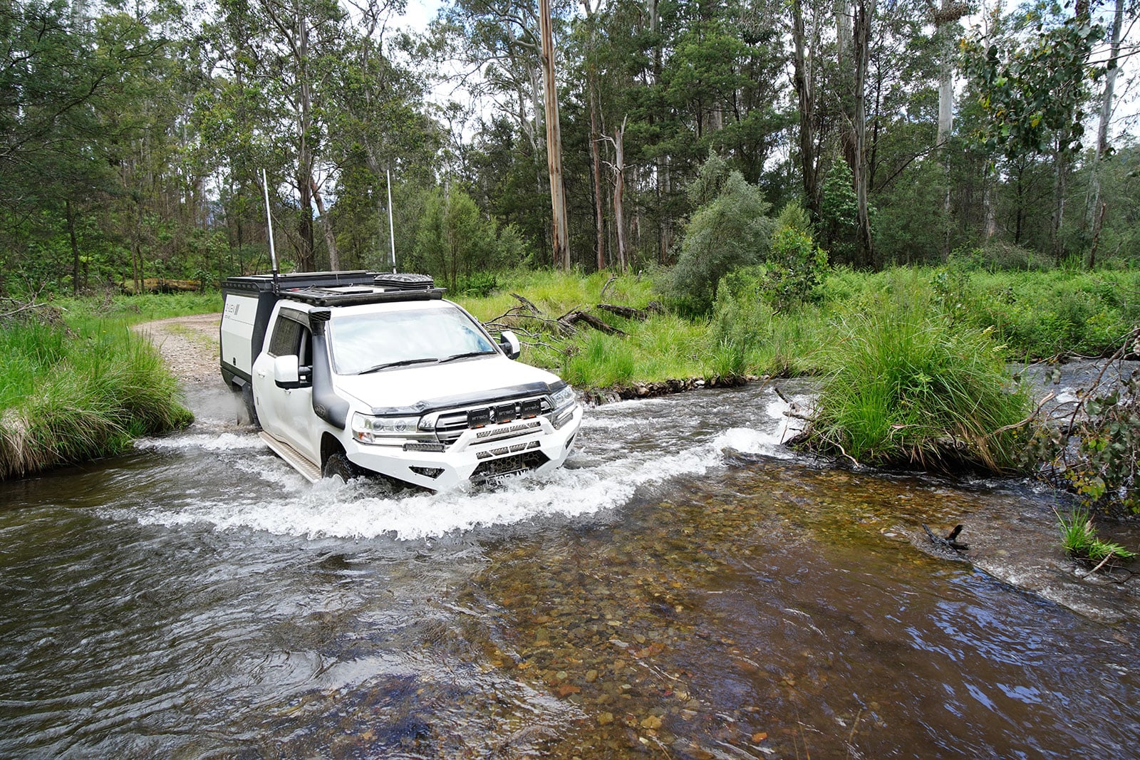 White off-road pickup crossing a shallow river in a forest with a rack on top and splash around the tires