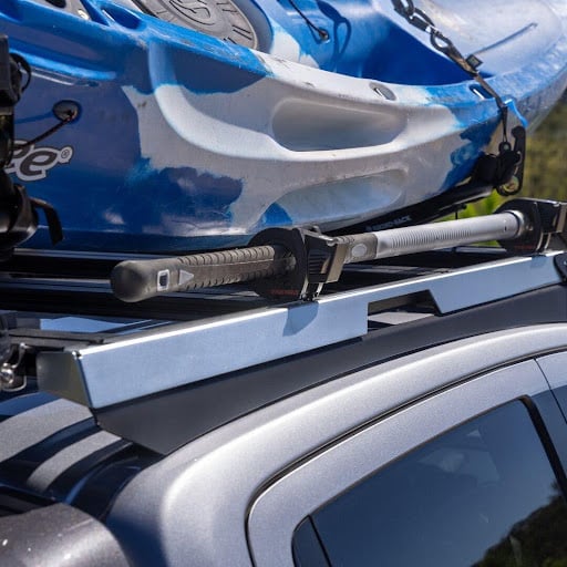 Blue kayak strapped to a roof rack on a car, with a paddle resting on the rack.