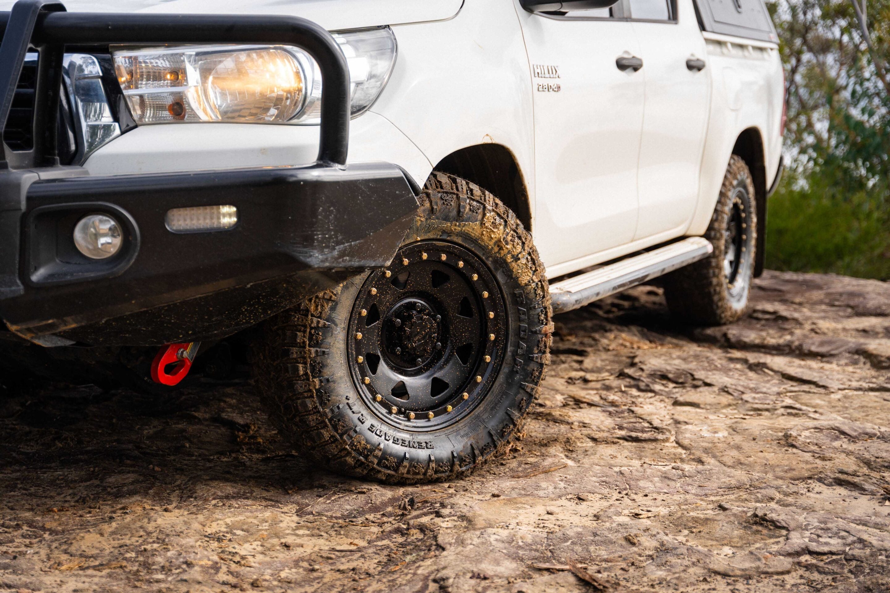White pickup truck with muddy off-road tires, front left wheel close-up on a dirt surface
