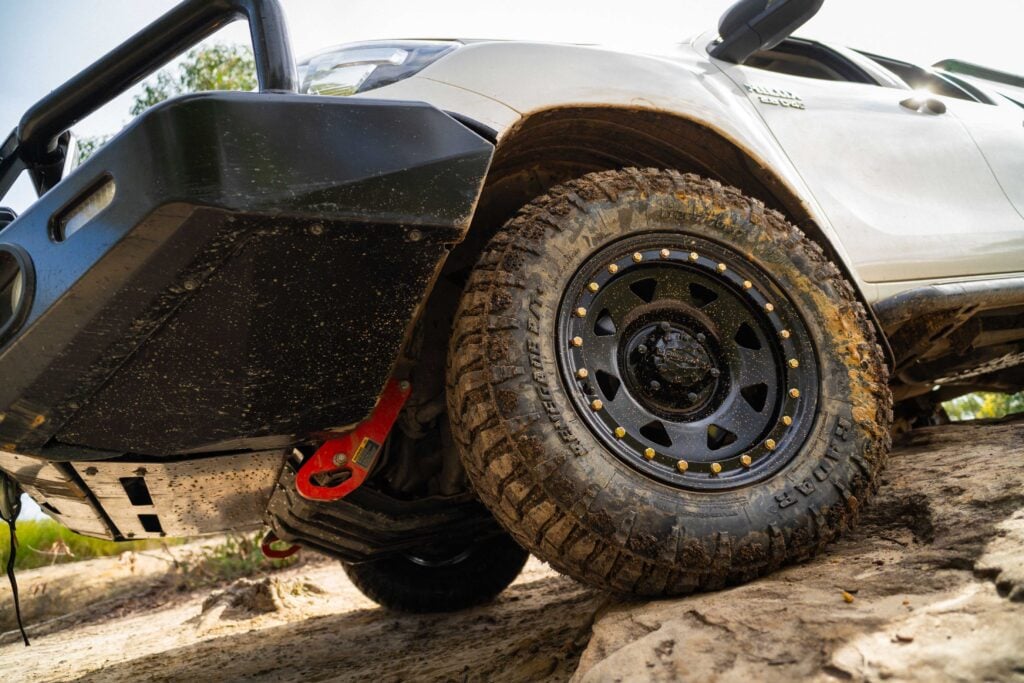 Close-up of a muddy off-road tire and black wheel on a lifted white SUV, with dirt splattered on the tread and fender.