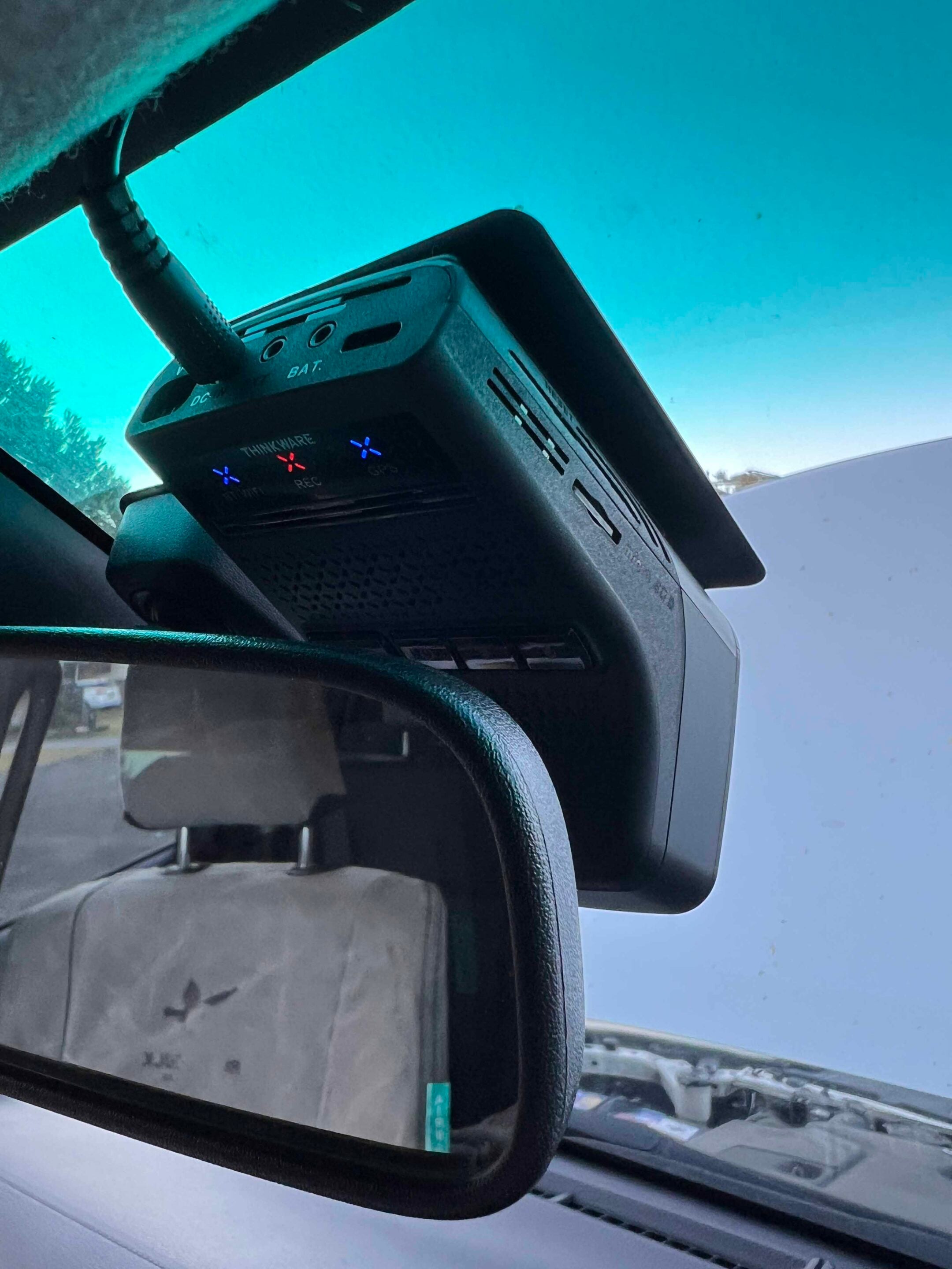 Dash cam mounted on the windshield inside a car, with the rearview mirror and blue sky visible through the windshield.