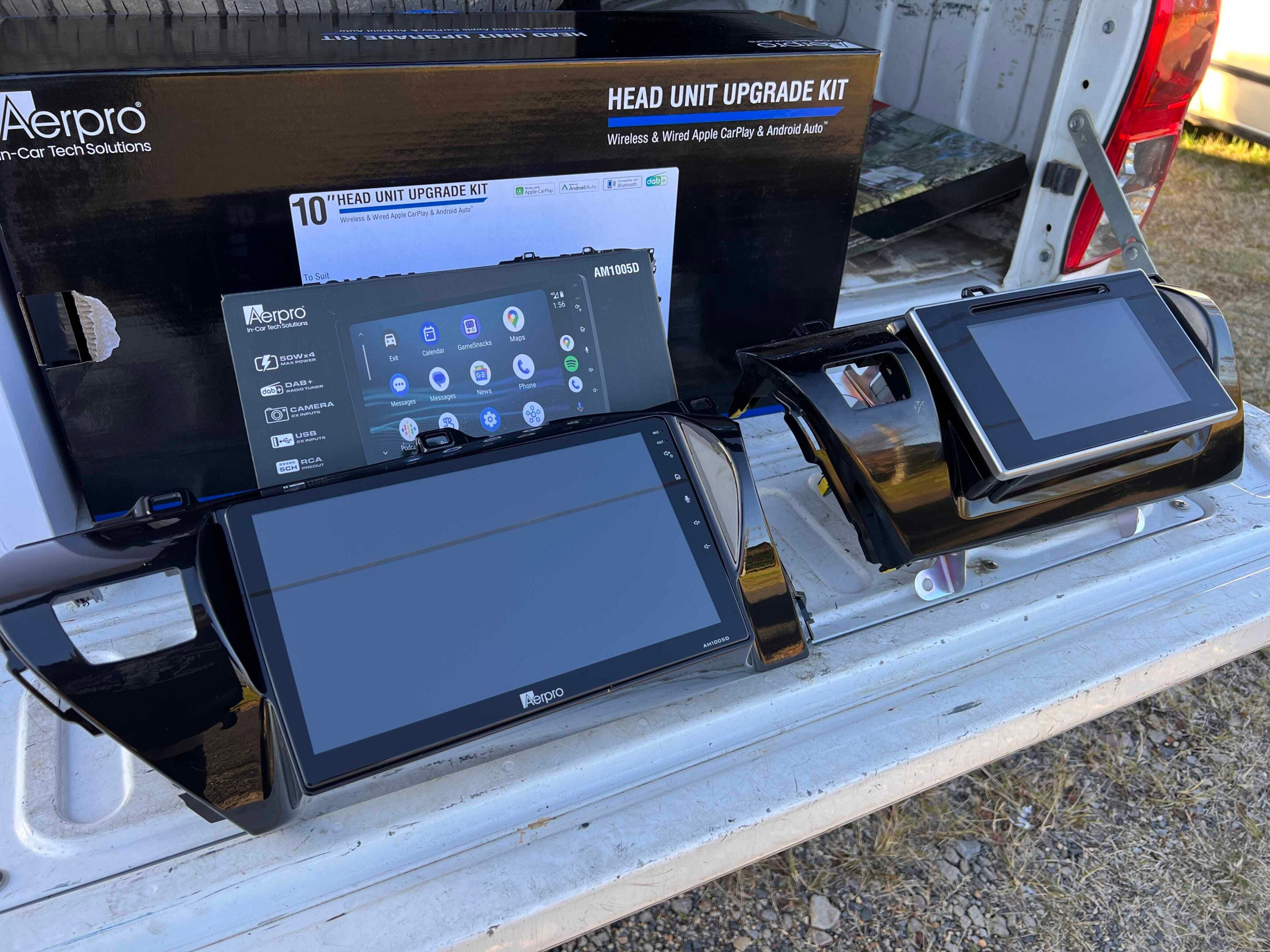 Boxed car head unit upgrade kit and several aftermarket displays laid out in a pickup truck bed, with Aerpro branding visible.