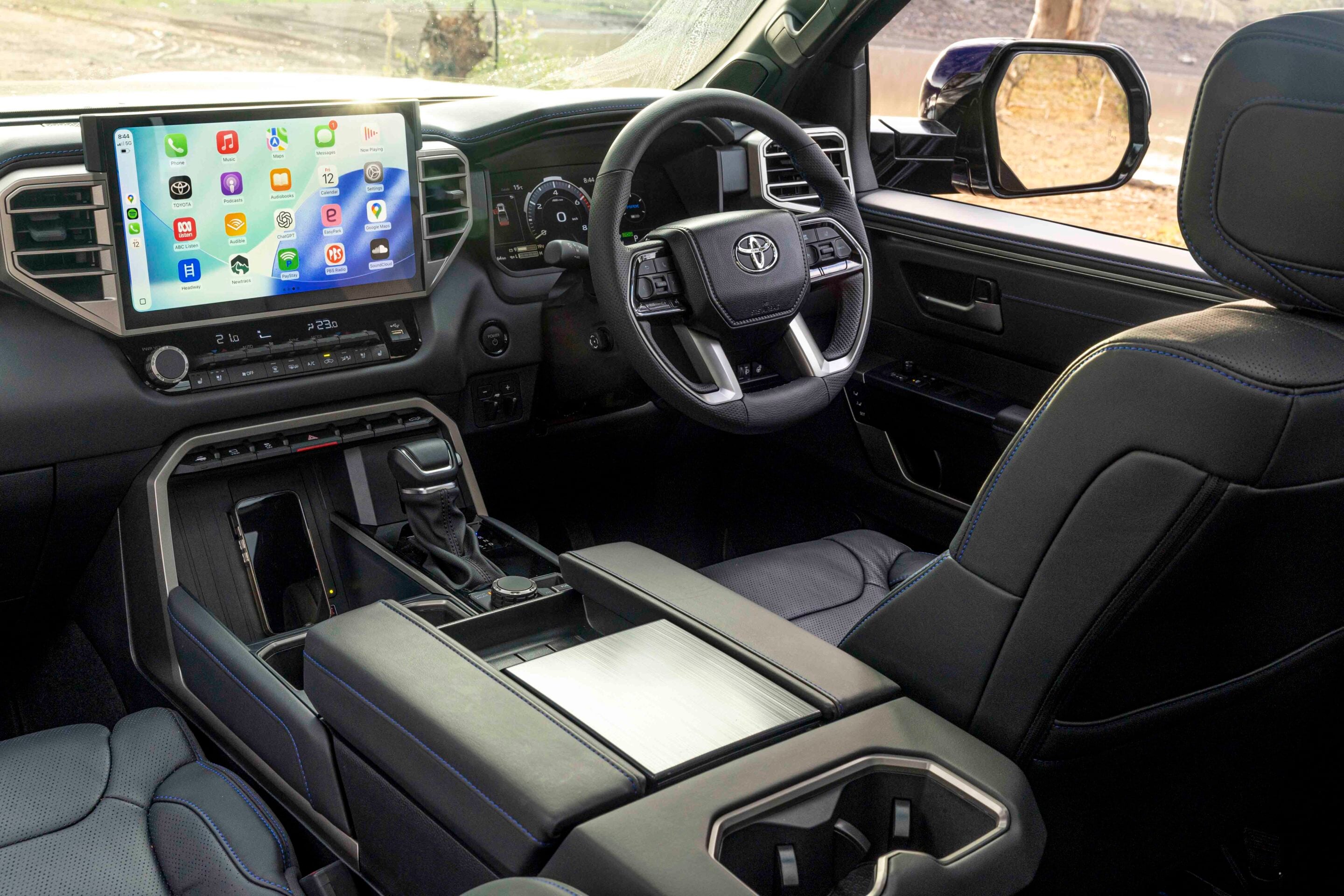 Modern car interior featuring a large tablet-style infotainment screen, steering wheel with Toyota emblem, and black leather seats with blue stitching.