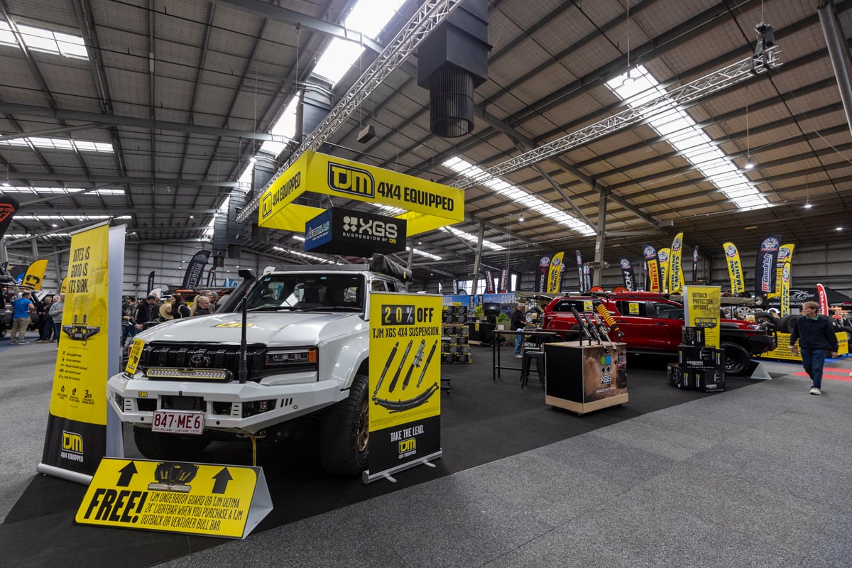 Exhibit booth for TJM 4x4 Equipped with a white off-road pickup on display and bright yellow promotional signs in a large indoor show hall, 20% off offer visible.