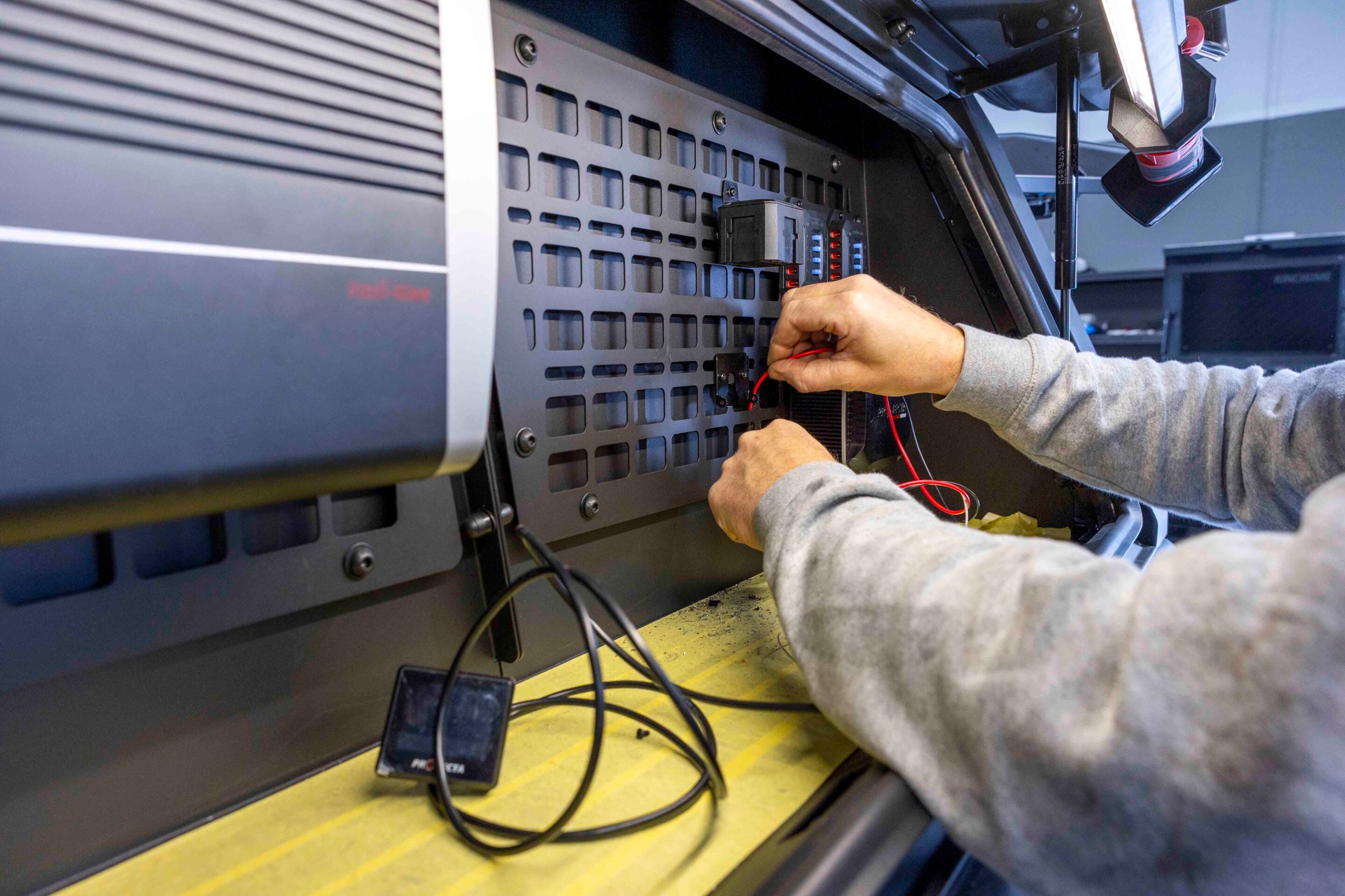 Technician wires red and black cables into a rack-mounted test panel inside a workshop.