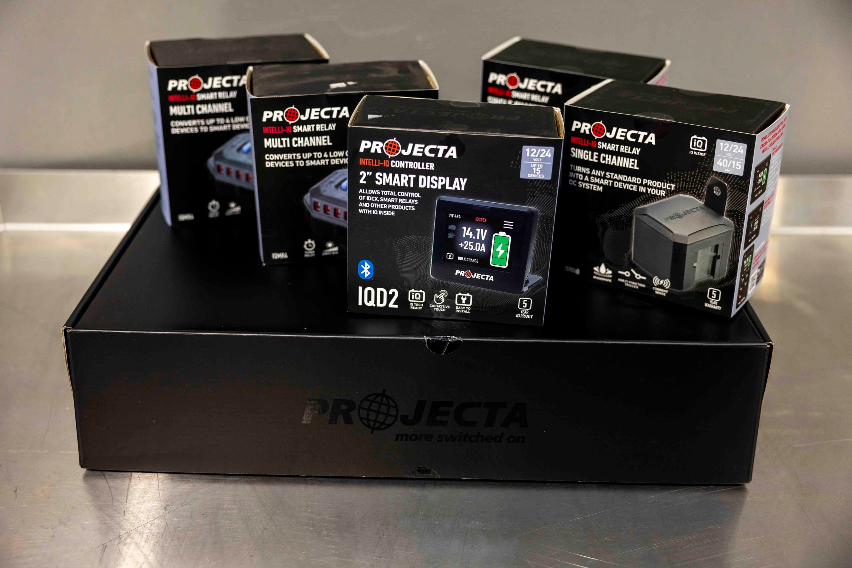 Assorted Projecta product boxes on a dark display box, featuring IQD2 smart display and multi-channel smart relay packaging.