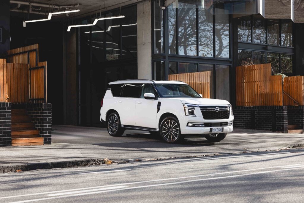 White SUV parked in front of a modern glass storefront with wooden fences on either side.