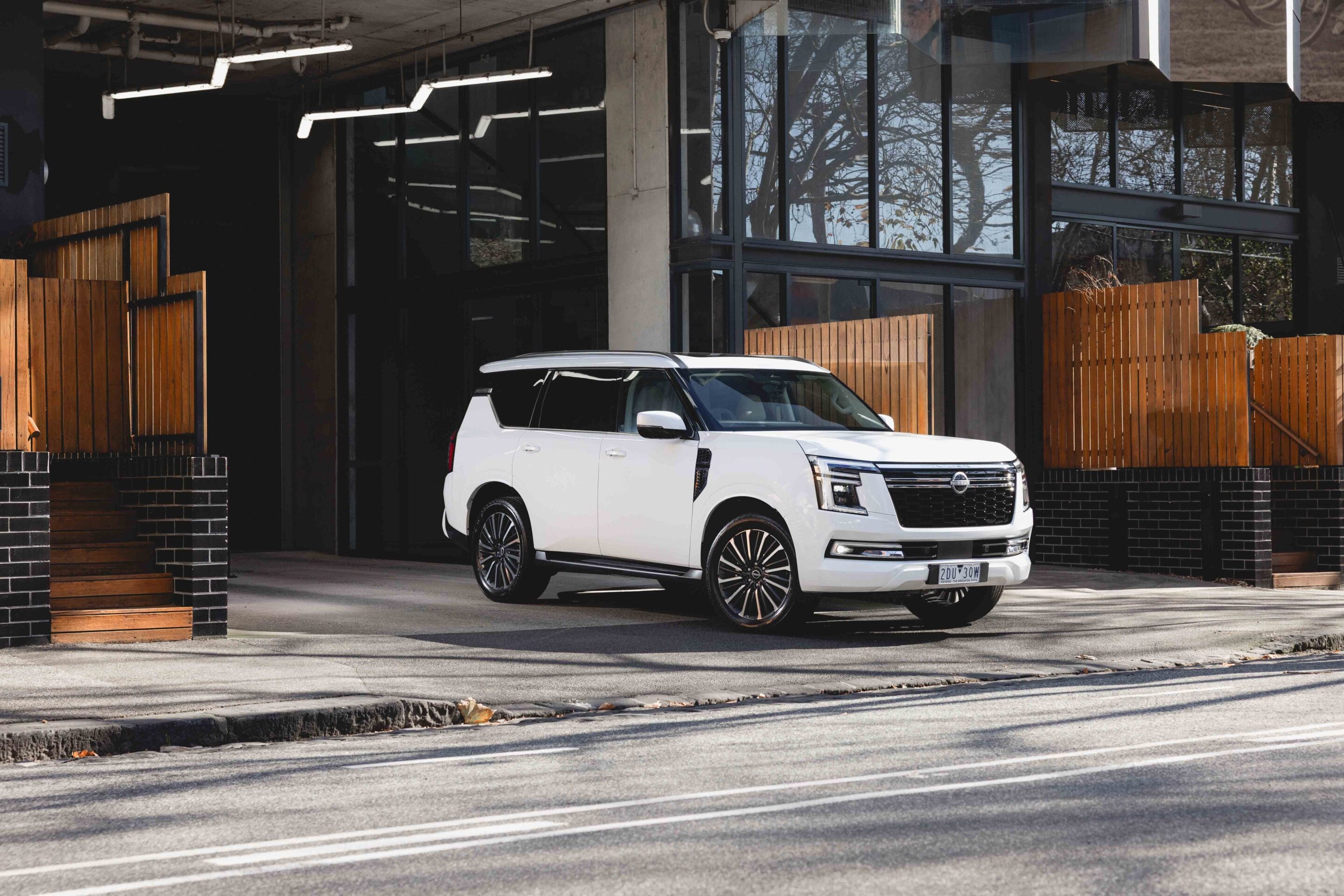 White SUV parked in front of a modern glass storefront with wooden fences on either side.