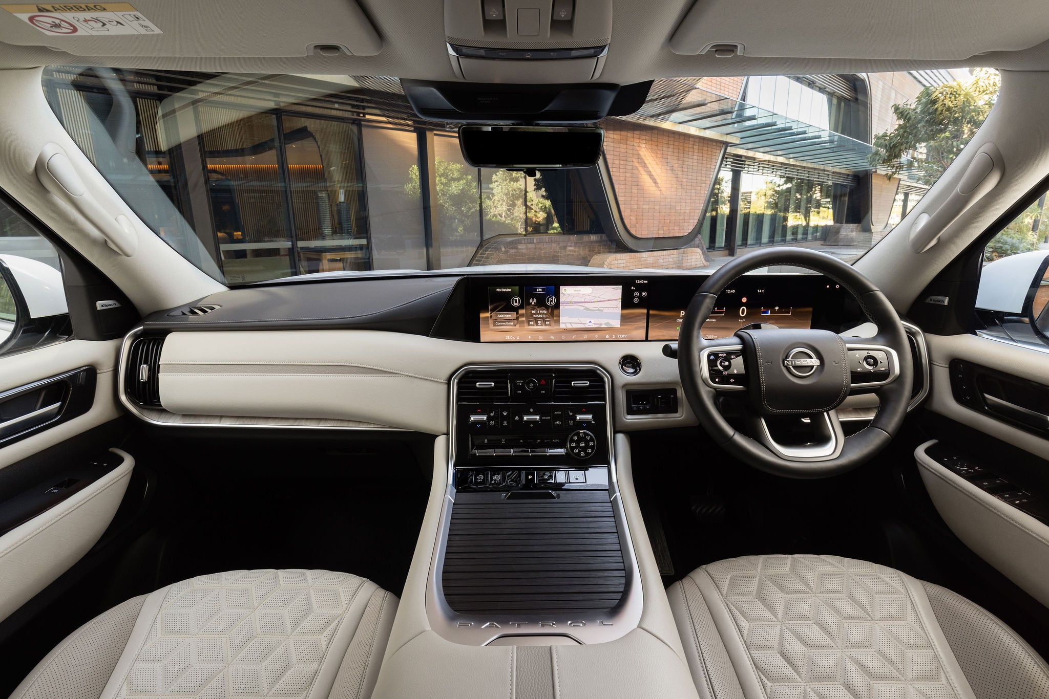 Interior of a luxury car with beige leather seats, a large digital dashboard, and a central touchscreen console viewed from the rear seat.