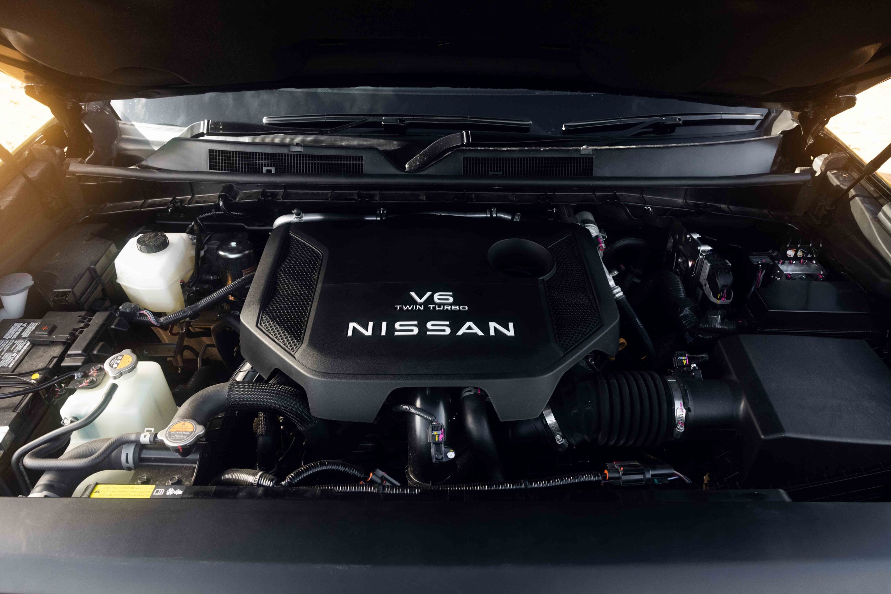 Engine bay of a Nissan vehicle featuring a V6 Twin Turbo engine cover with Nissan branding visible.