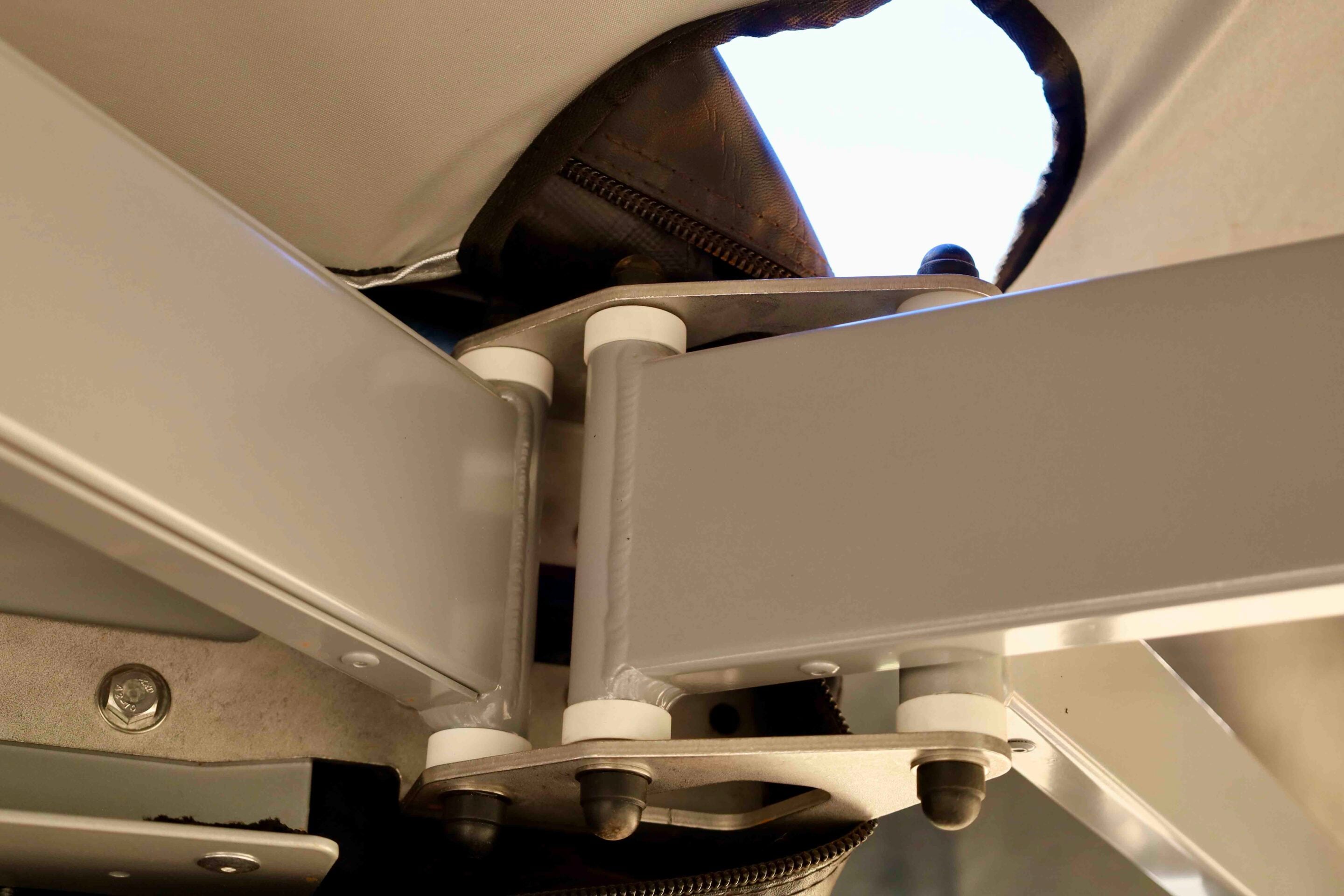 Close-up of a metal hinge/ pivot mechanism with white rollers and a textured strap inside a gray metal frame.