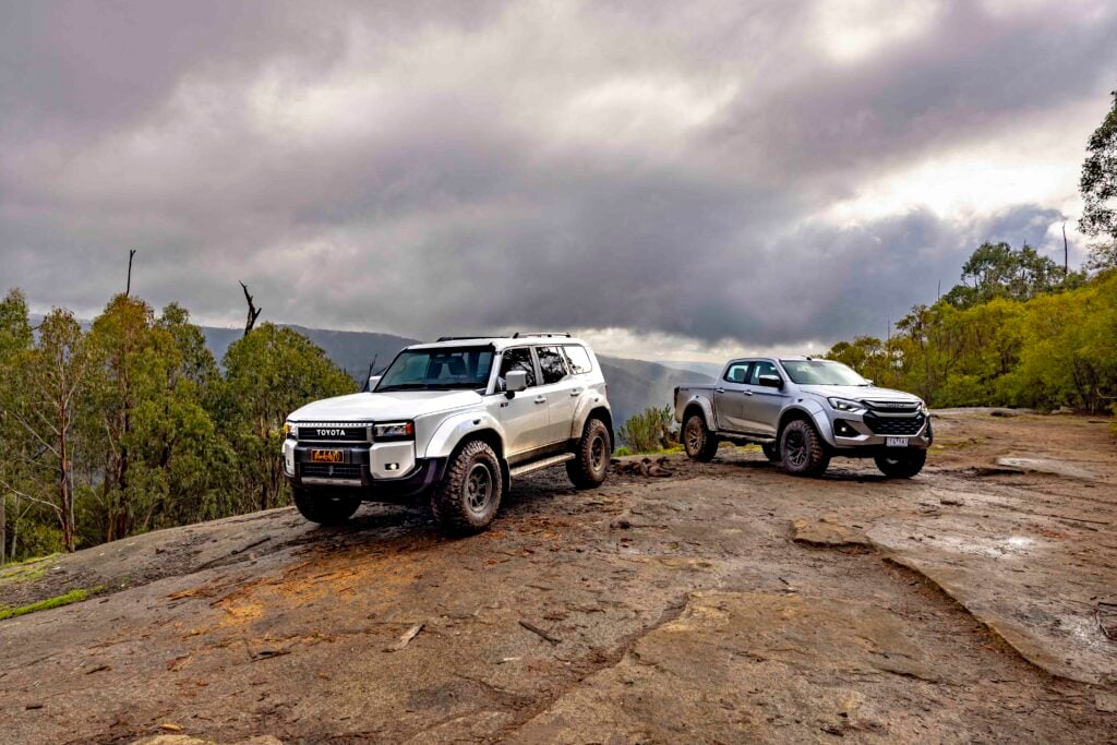 Two pickups parked on a rocky overlook under a cloudy sky with forested hills in the distance.