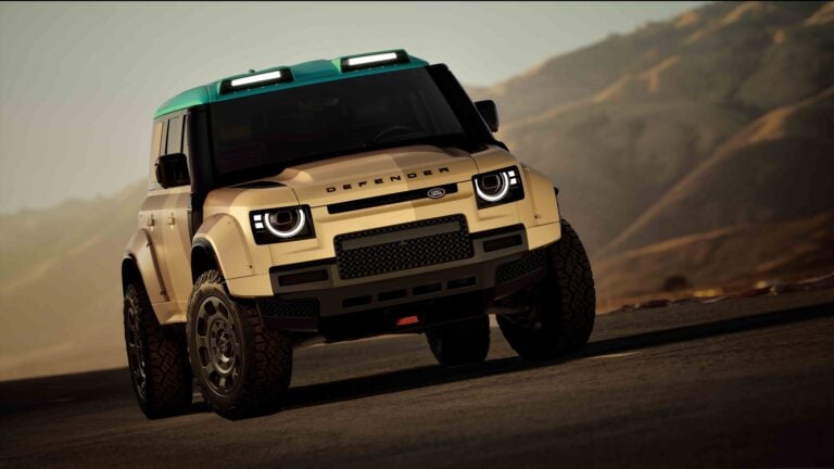 Beige Land Rover Defender with a green roof driving on a rocky desert road, angled from the front-left.