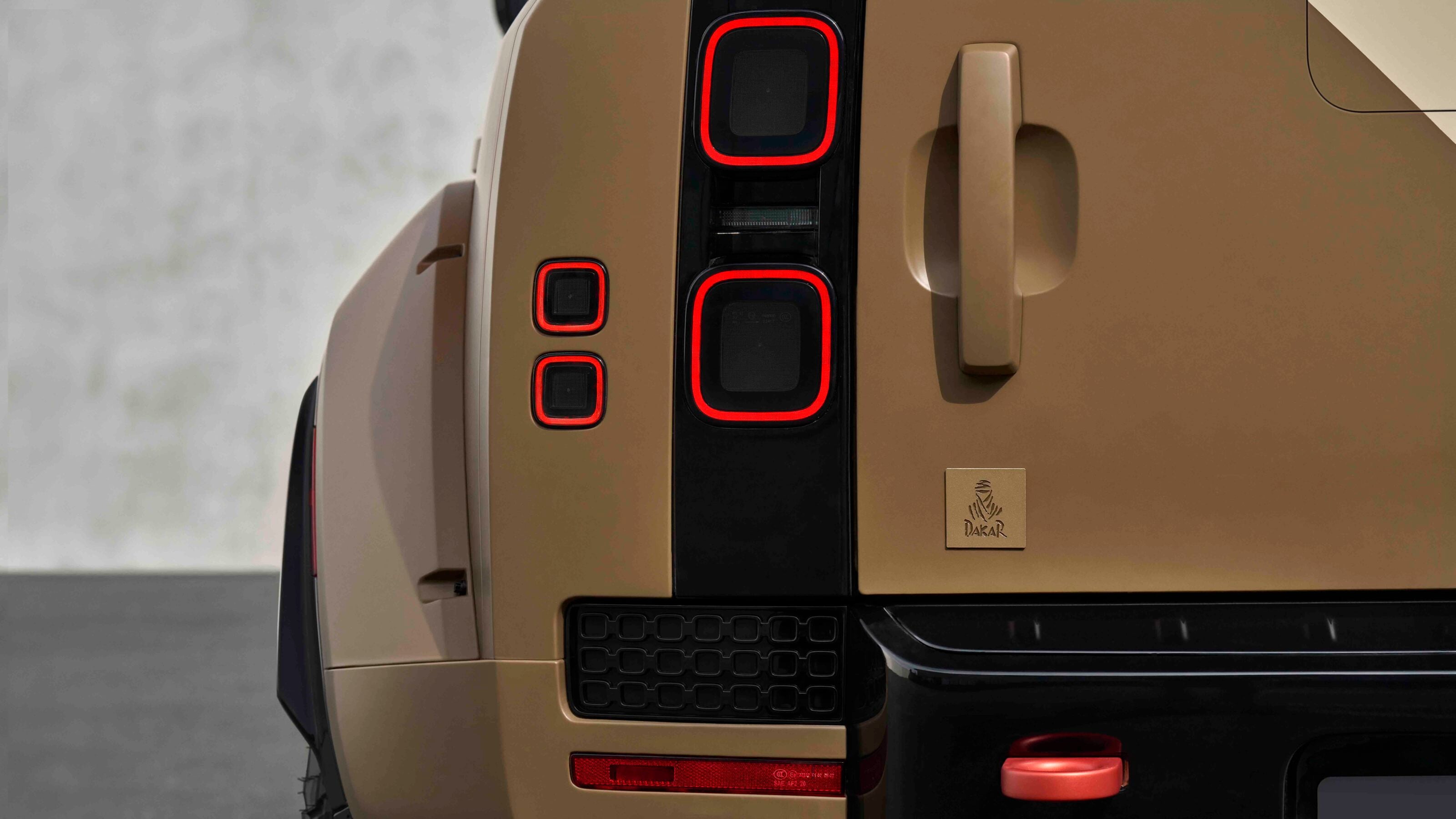 Rear of a tan Dakar off-road vehicle showing vertical red-ring tail lights, beige tailgate handle, and Dakar badge.