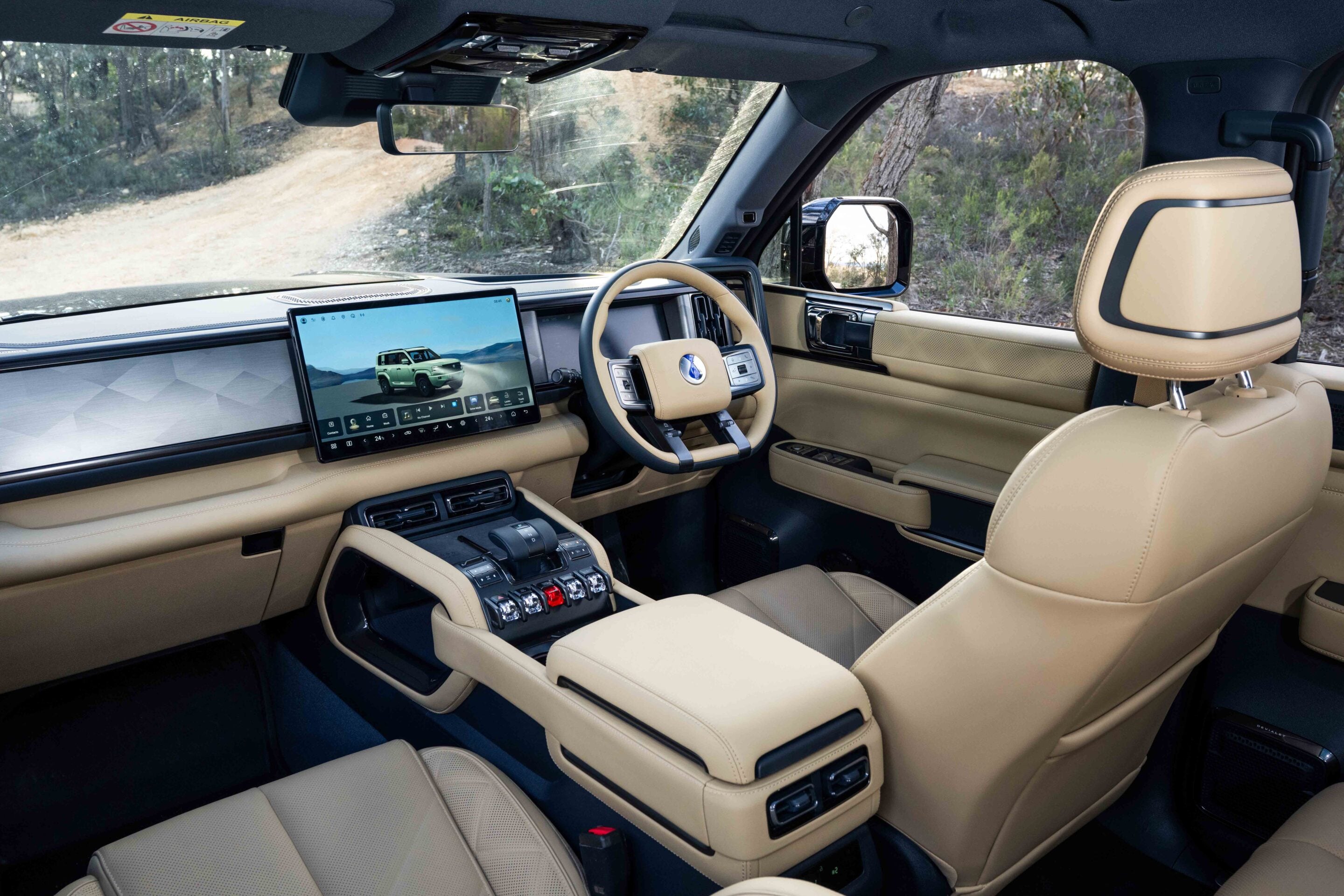 Interior of a luxury SUV with beige leather seats, a wide tablet-style infotainment screen, and center console controls visible from the front passenger area.