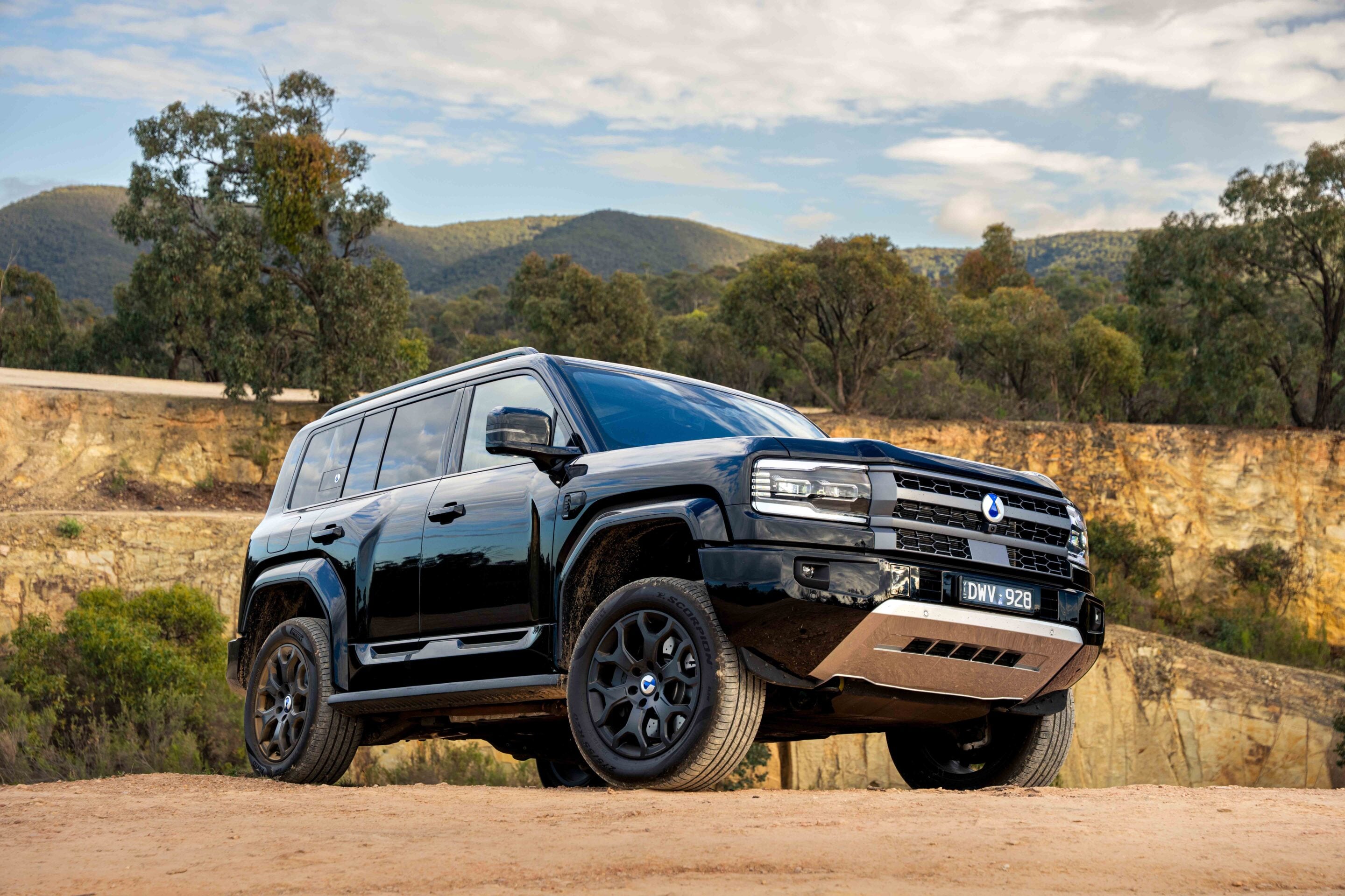 Black SUV parked on a dirt road with a rocky wall and hills in the background under a cloudy blue sky