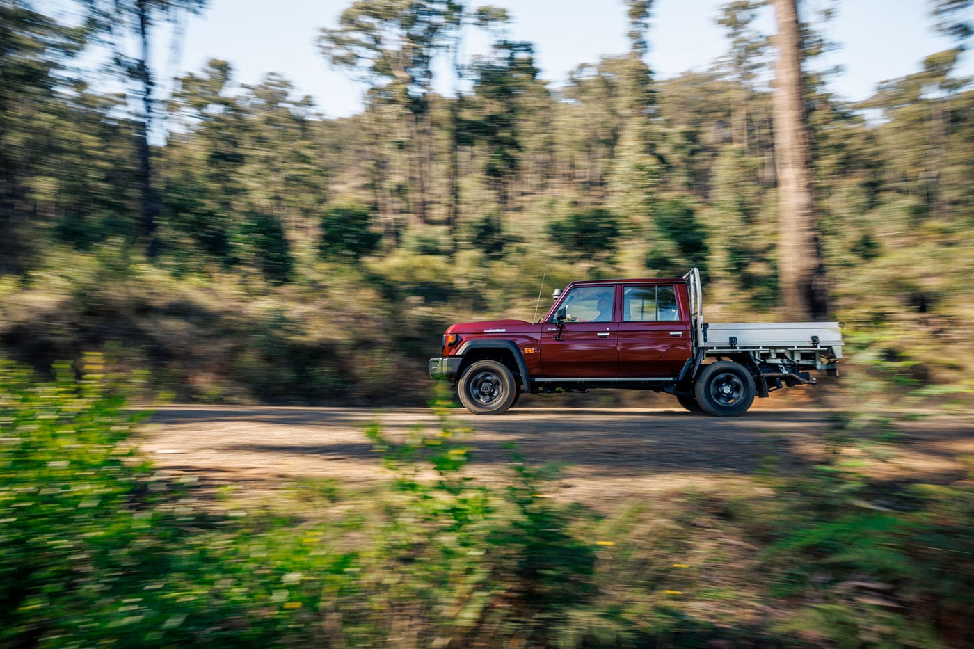 Red pickup truck driving along a dirt forest road with trees blurred from motion.