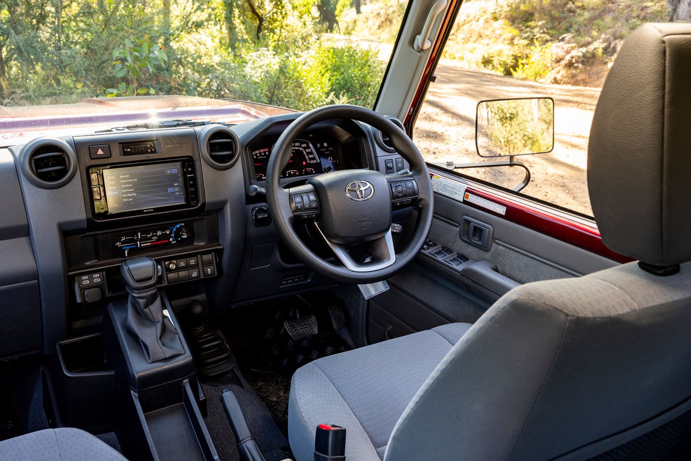 Interior view of a vehicle cabin with steering wheel, dashboard, and gear shifter; scenery visible through the windshield black SUV/Off-road trail outside