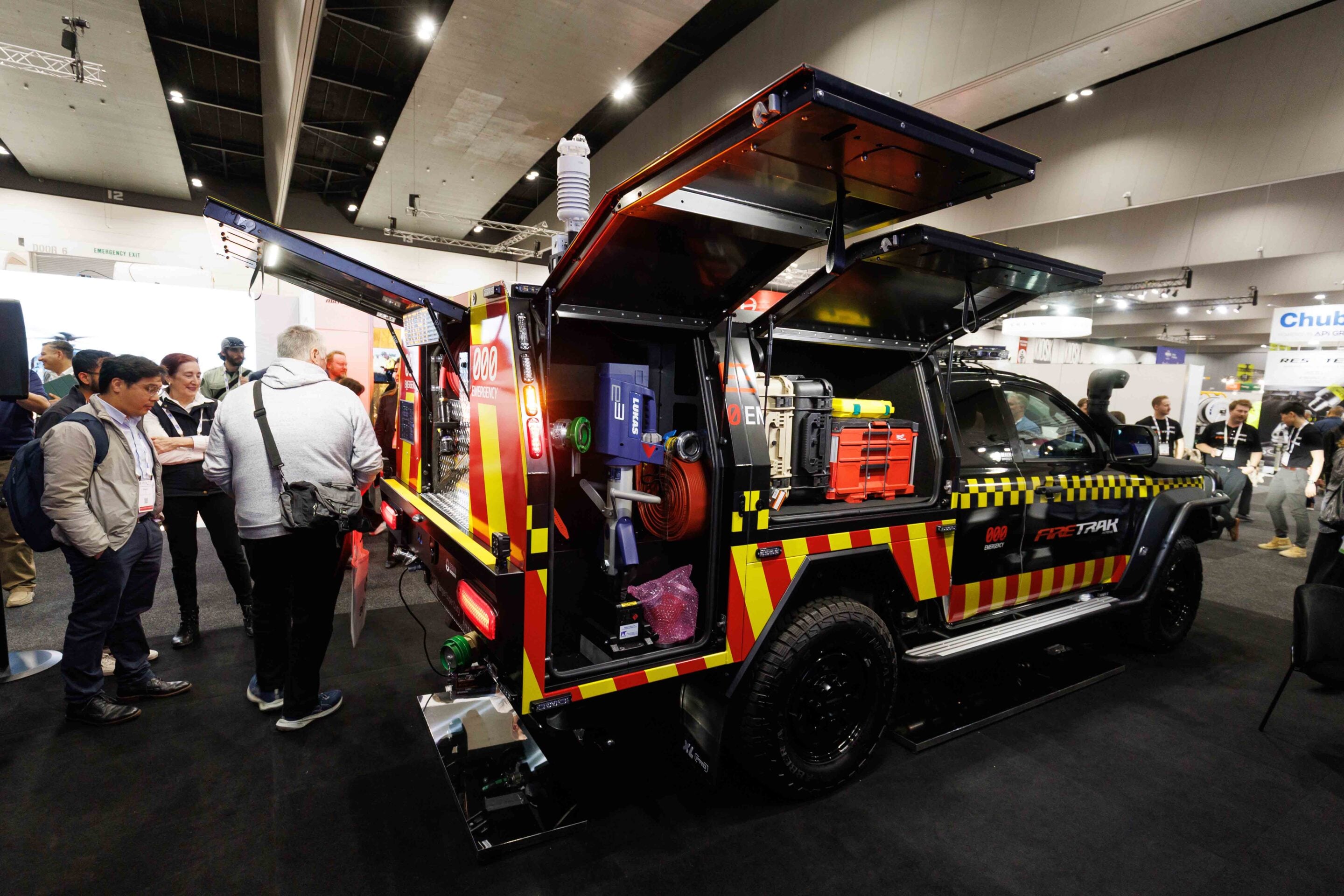 Attendees at an expo viewing a brightly colored emergency response vehicle with open equipment bays.