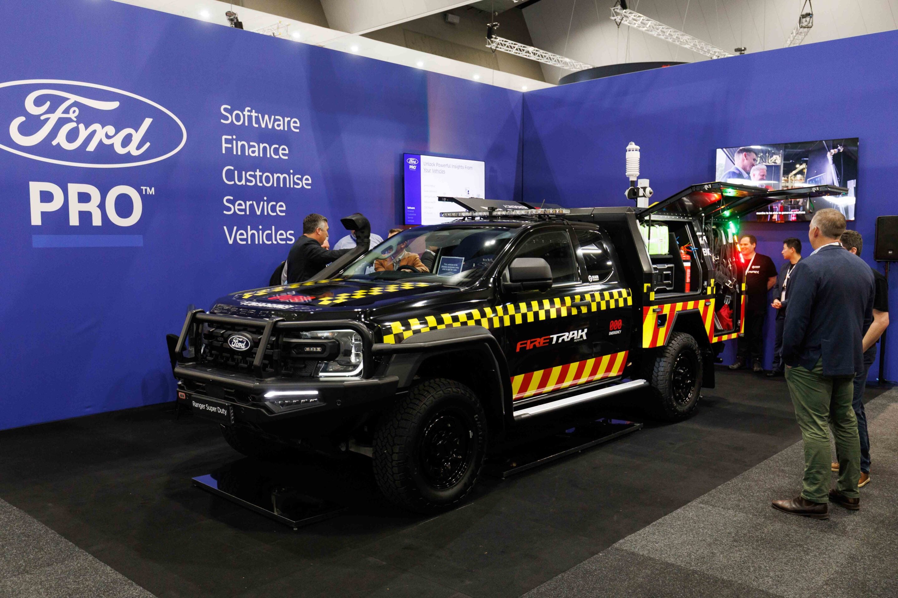 Ford Pro exhibition booth with a black emergency vehicle on display and visitors nearby.