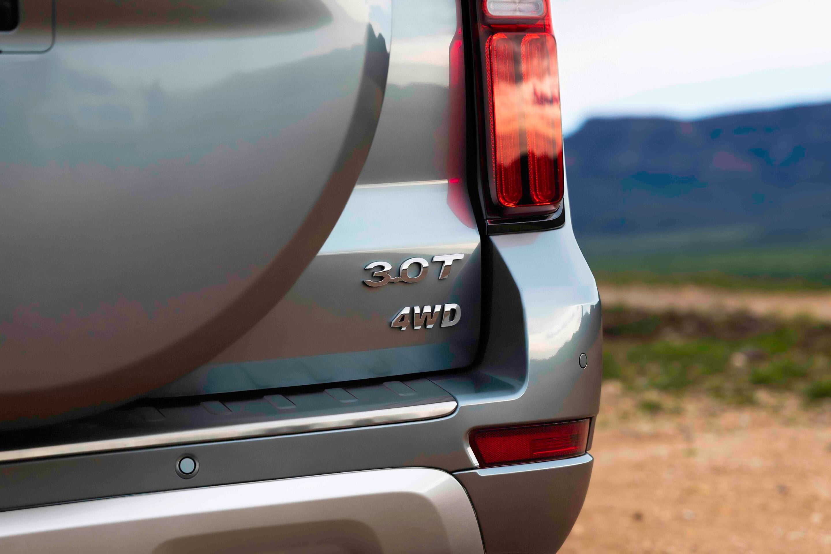 Rear view of a silver SUV showing the '3.0T' and '4WD' badges near a red vertical tail light, outdoors.