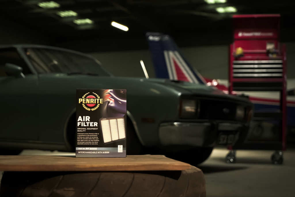Penrite air filter box on a wooden table in a dim garage with a classic car and a red tool cabinet in the background.