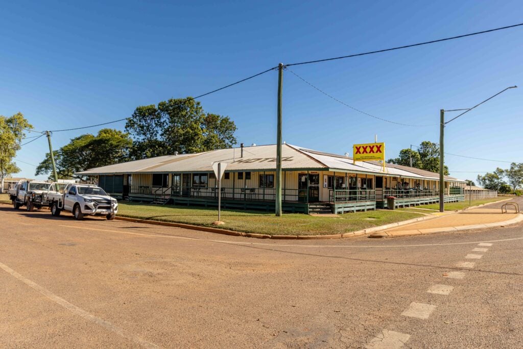 One-story motel with a yellow XXX sign along a street, blue sky overhead and several parked cars in front.
