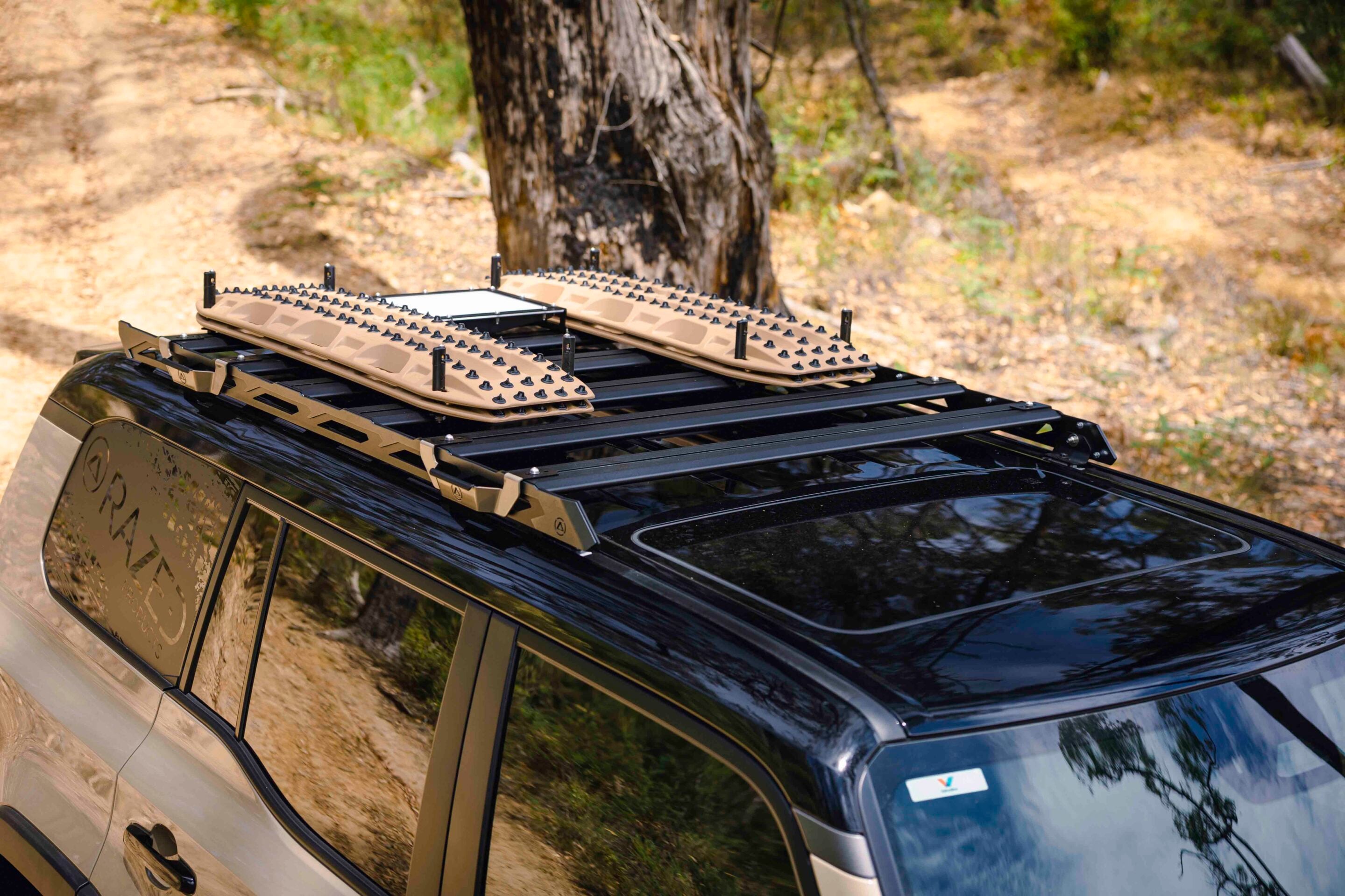 SUV with roof rack carrying tan traction boards on a dirt trail in a forested area