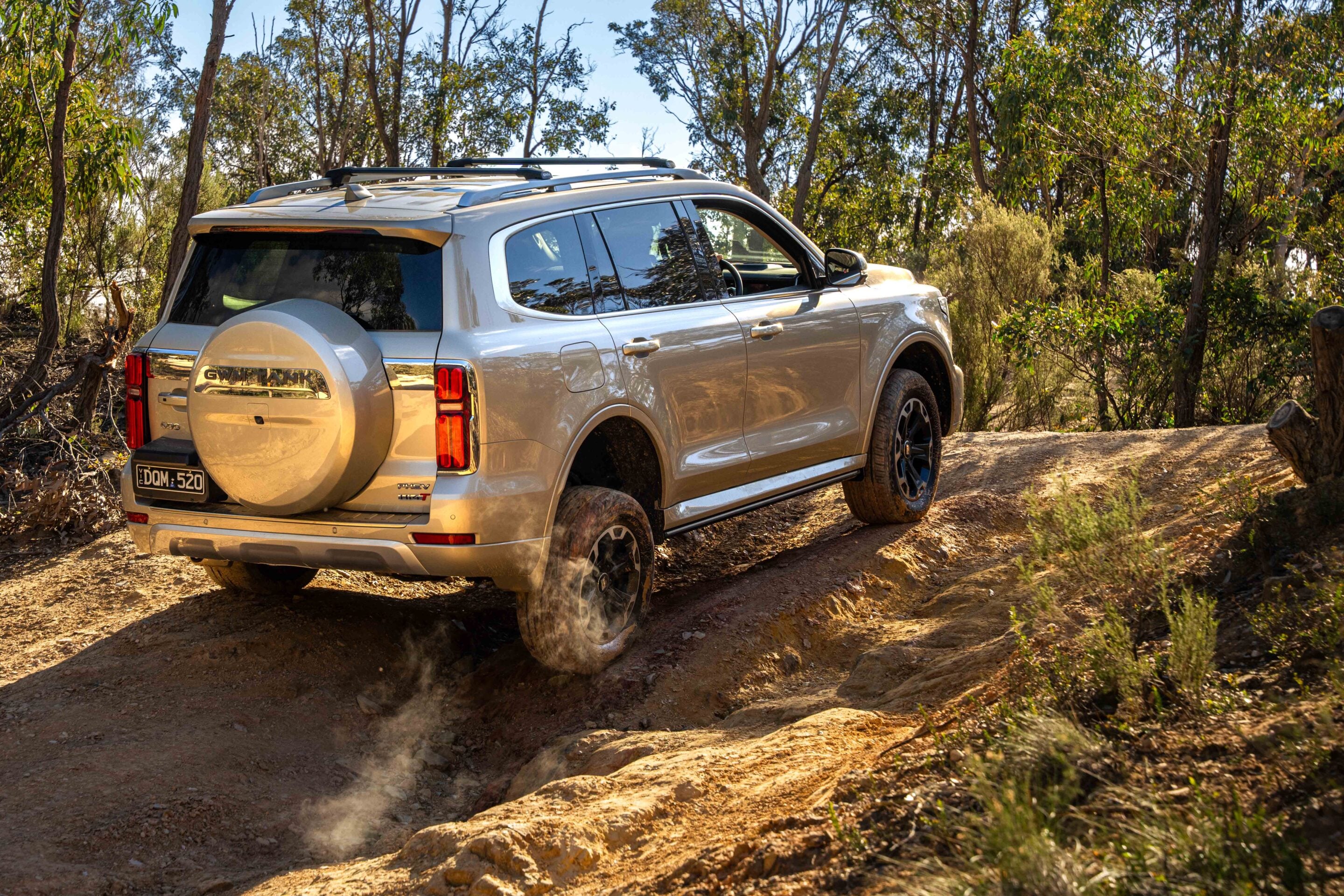 White SUV driving off-road along a dusty dirt trail in a forest, kicking up dust behind it