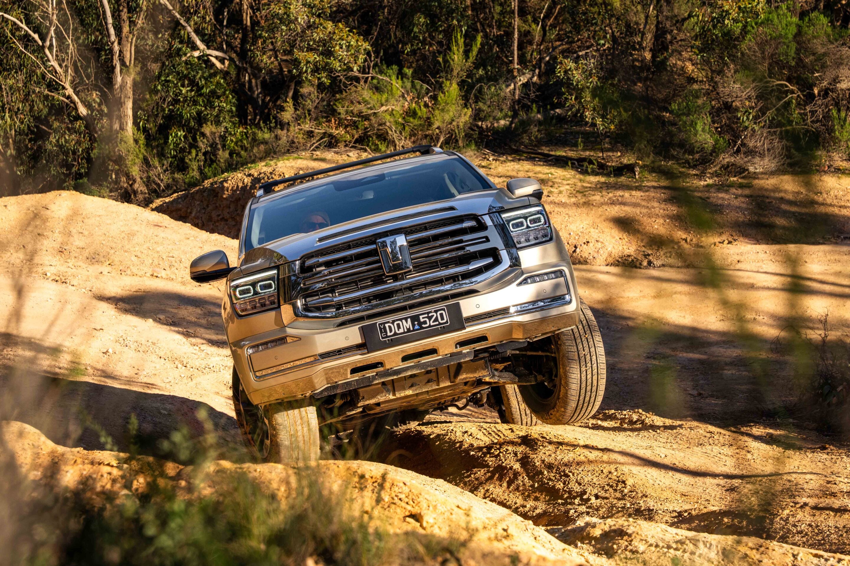 Silver pickup truck driving up a rocky dirt trail with dense forest in the background.