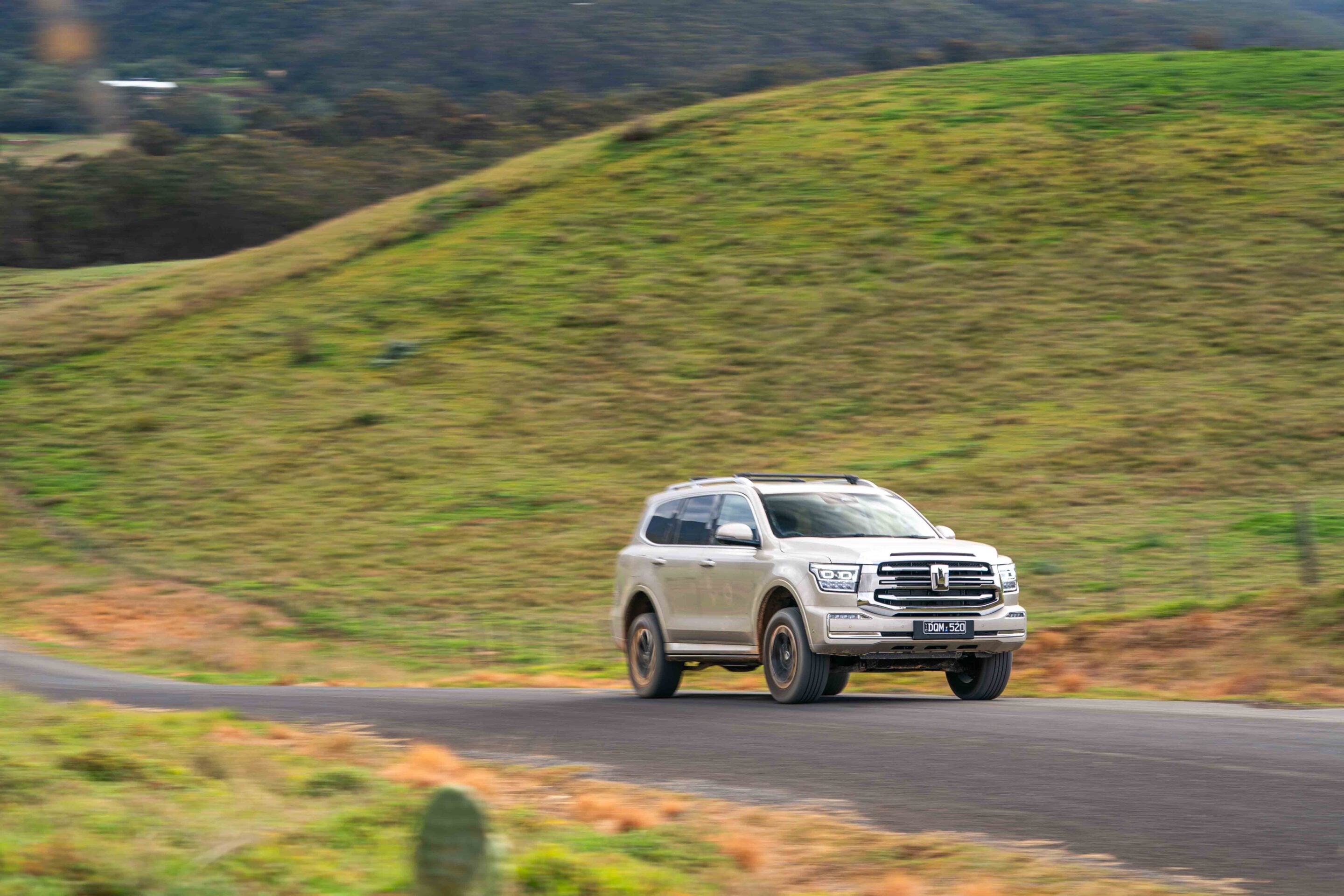 Silver SUV driving along a curved road with grassy hills in the background, motion blur.