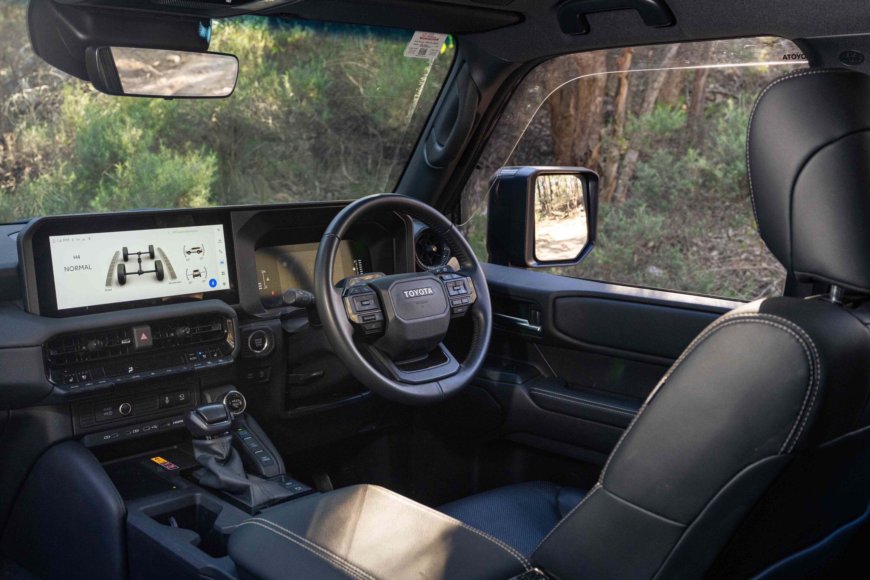 Interior of a modern SUV—steering wheel, large central touchscreen, digital gauges, and driver-side mirror visible through the cabin window.
