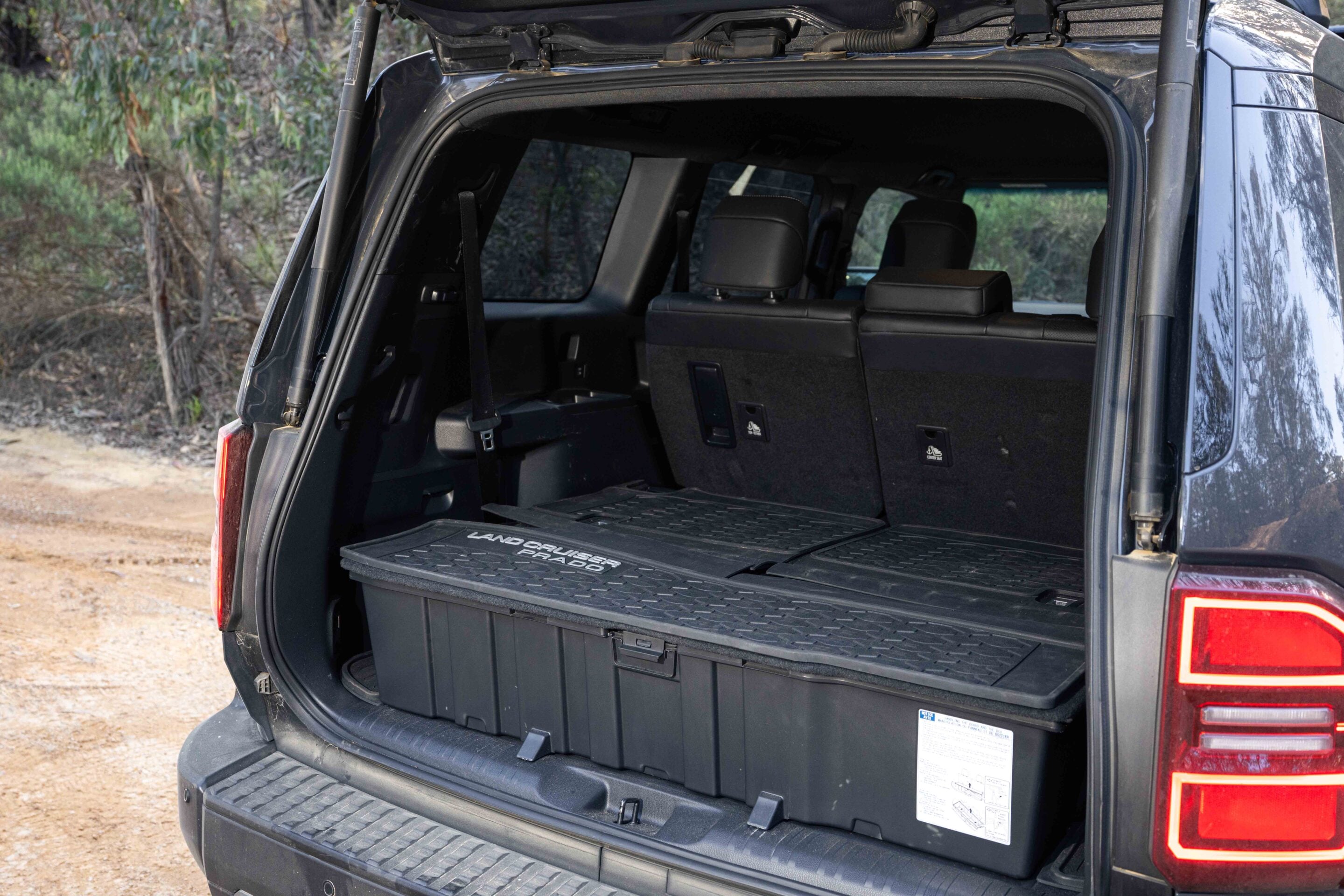 Open rear of a dark SUV with the tailgate up, revealing a large black storage box in the cargo area and visible upright second-row seats behind it.