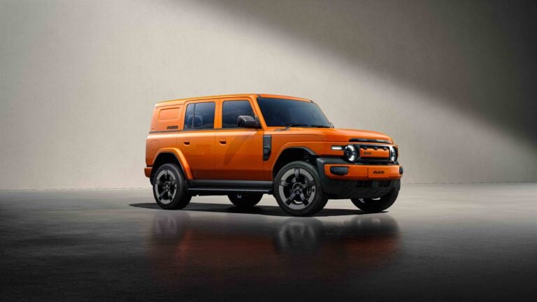 Orange off-road SUV in a studio setting with a gradient wall and reflective floor, facing left.