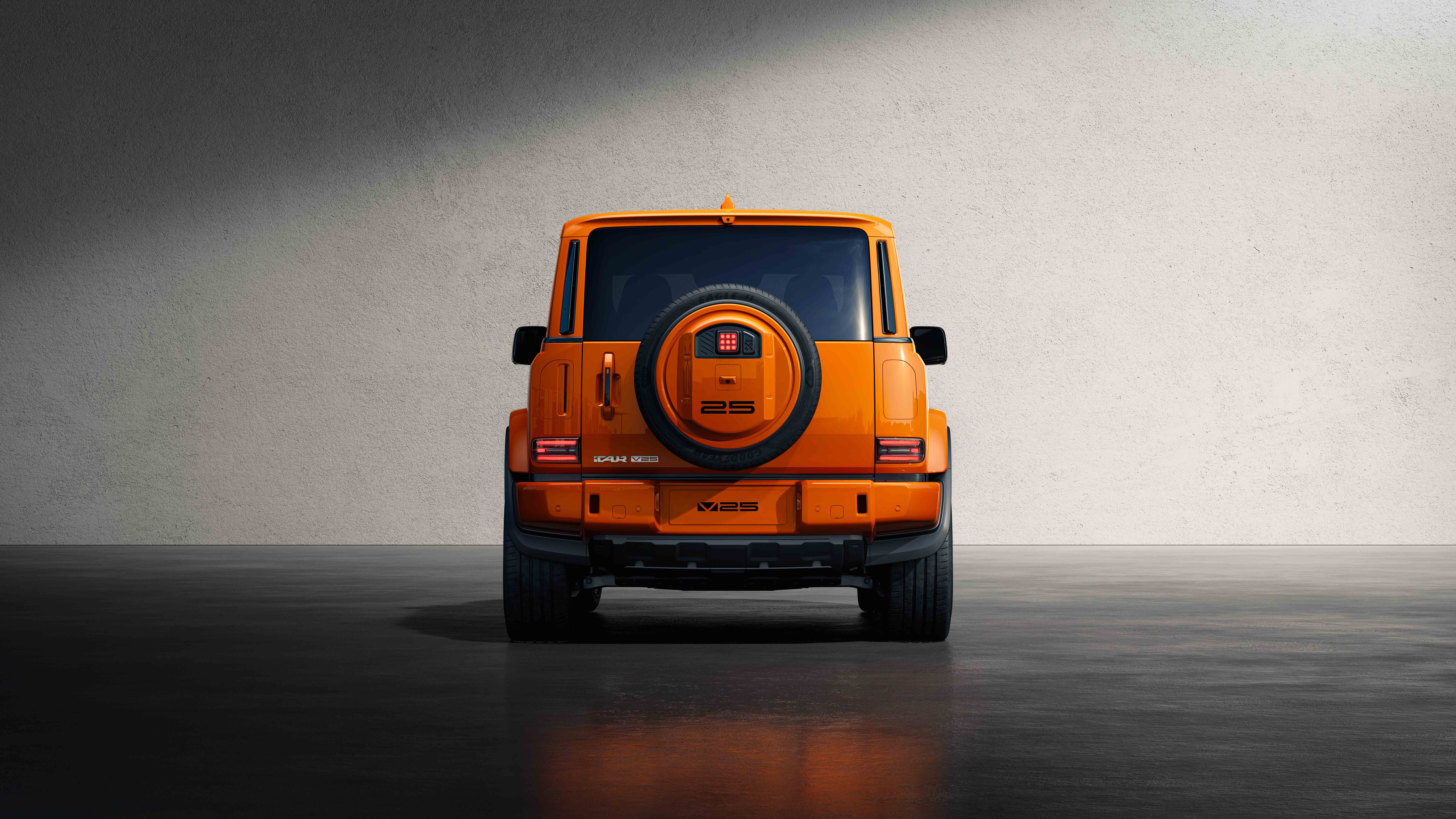 Rear view of an orange off-road SUV with a spare tire mounted on the back, parked against a textured gray wall.
