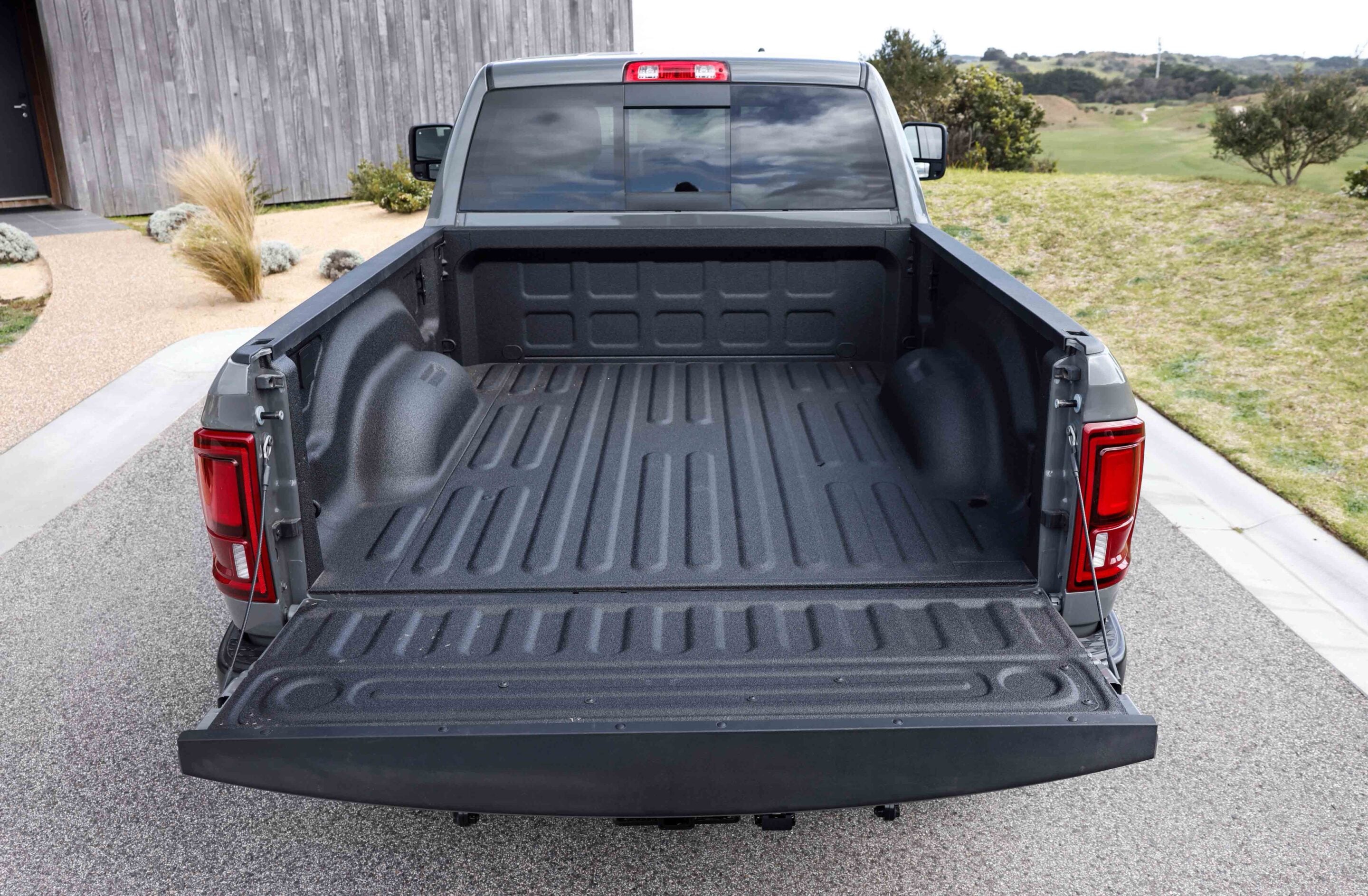 Rear view of a dark gray pickup truck with the tailgate down and an empty cargo bed on a driveway by a modern house.