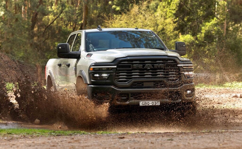 White RAM pickup driving through a muddy puddle in a forest, mud spraying around.