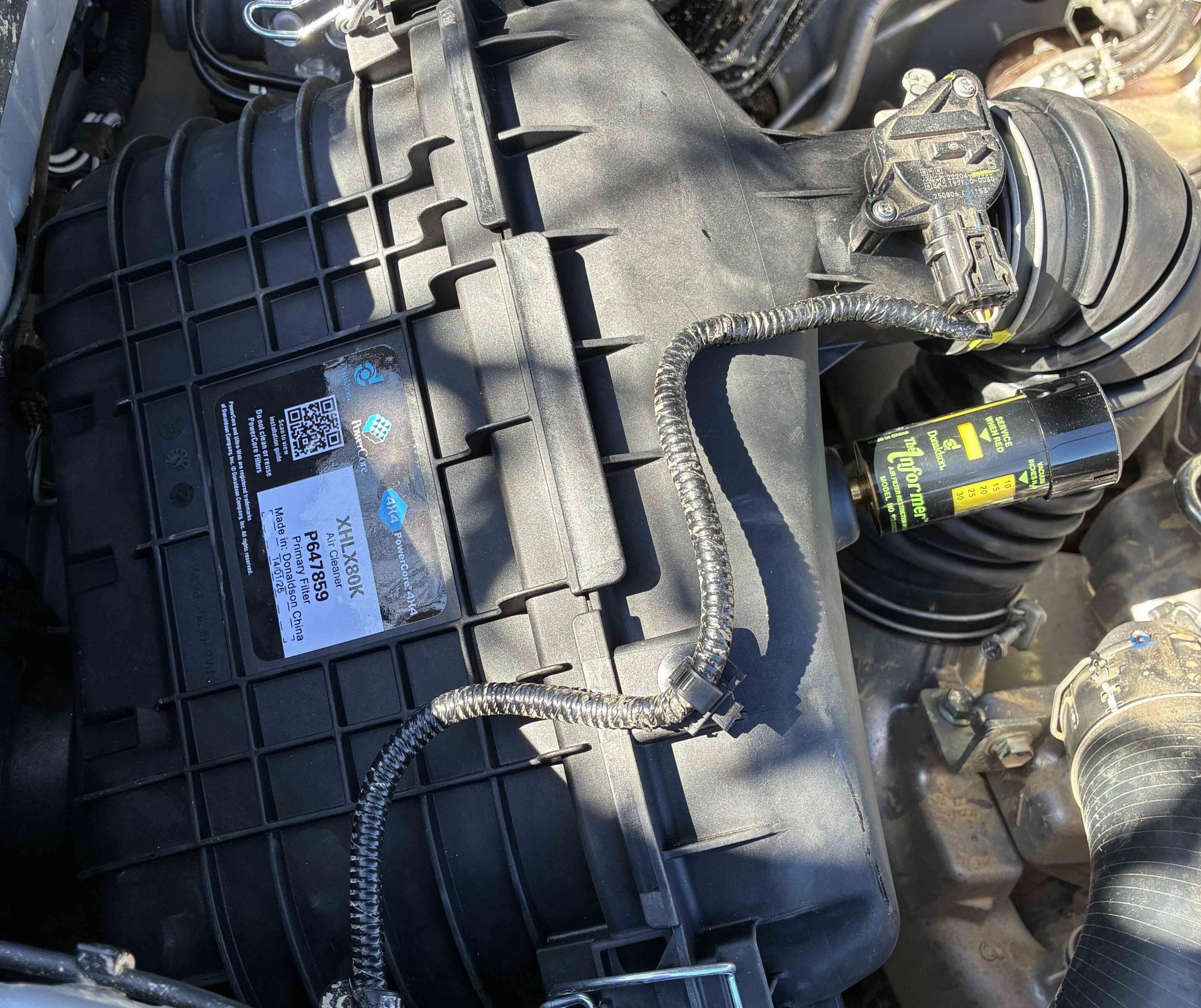 Close-up of a car's plastic air intake housing with wiring harnesses and connectors visible near the engine bay sticker.