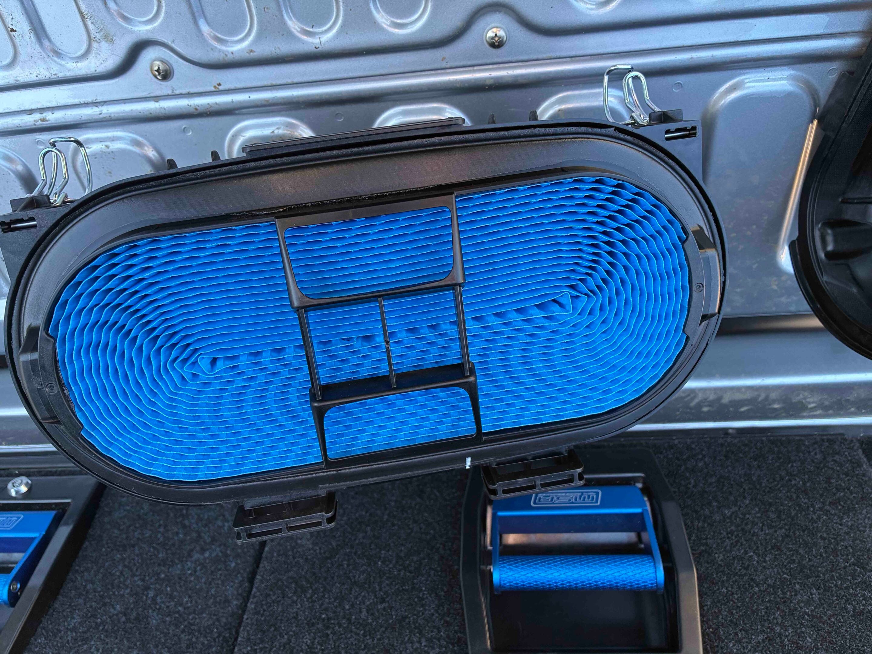 Open car trunk showing a blue, pleated cabin air filter partially pulled out of its housing.