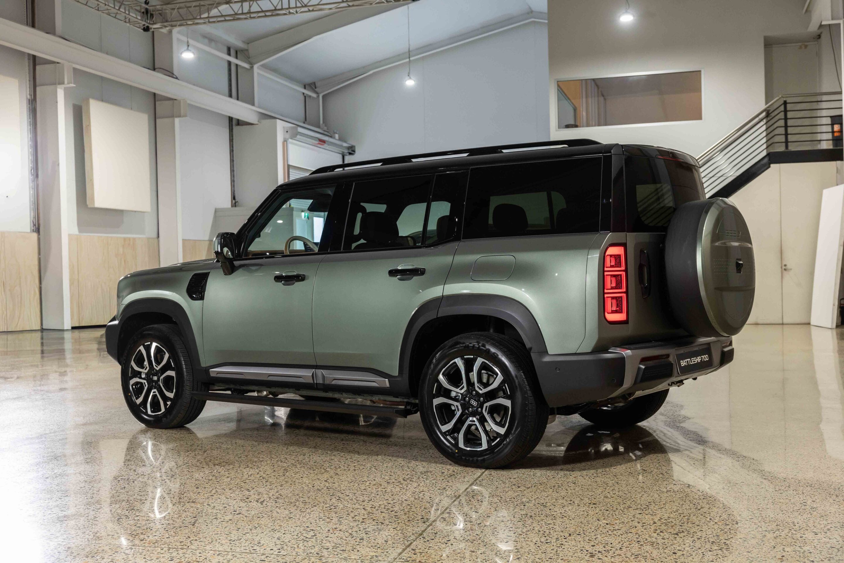 Green SUV with a mounted spare tire on the rear door, parked inside a bright showroom with polished floors and overhead lighting.