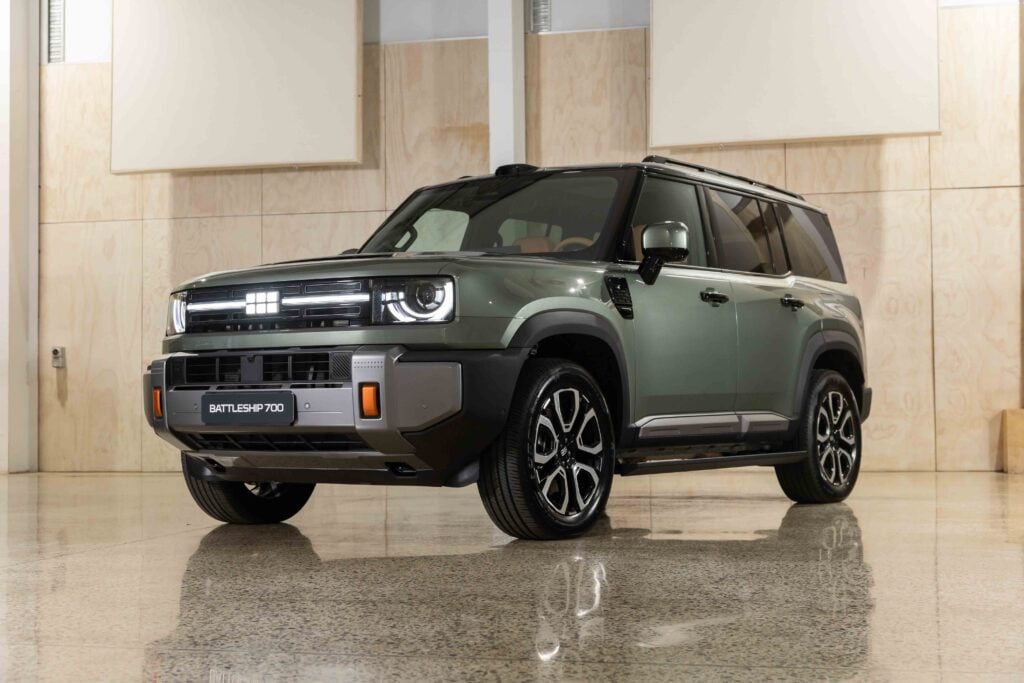 Front three-quarter view of a green Land Rover Defender Battleship 700 in a bright showroom.