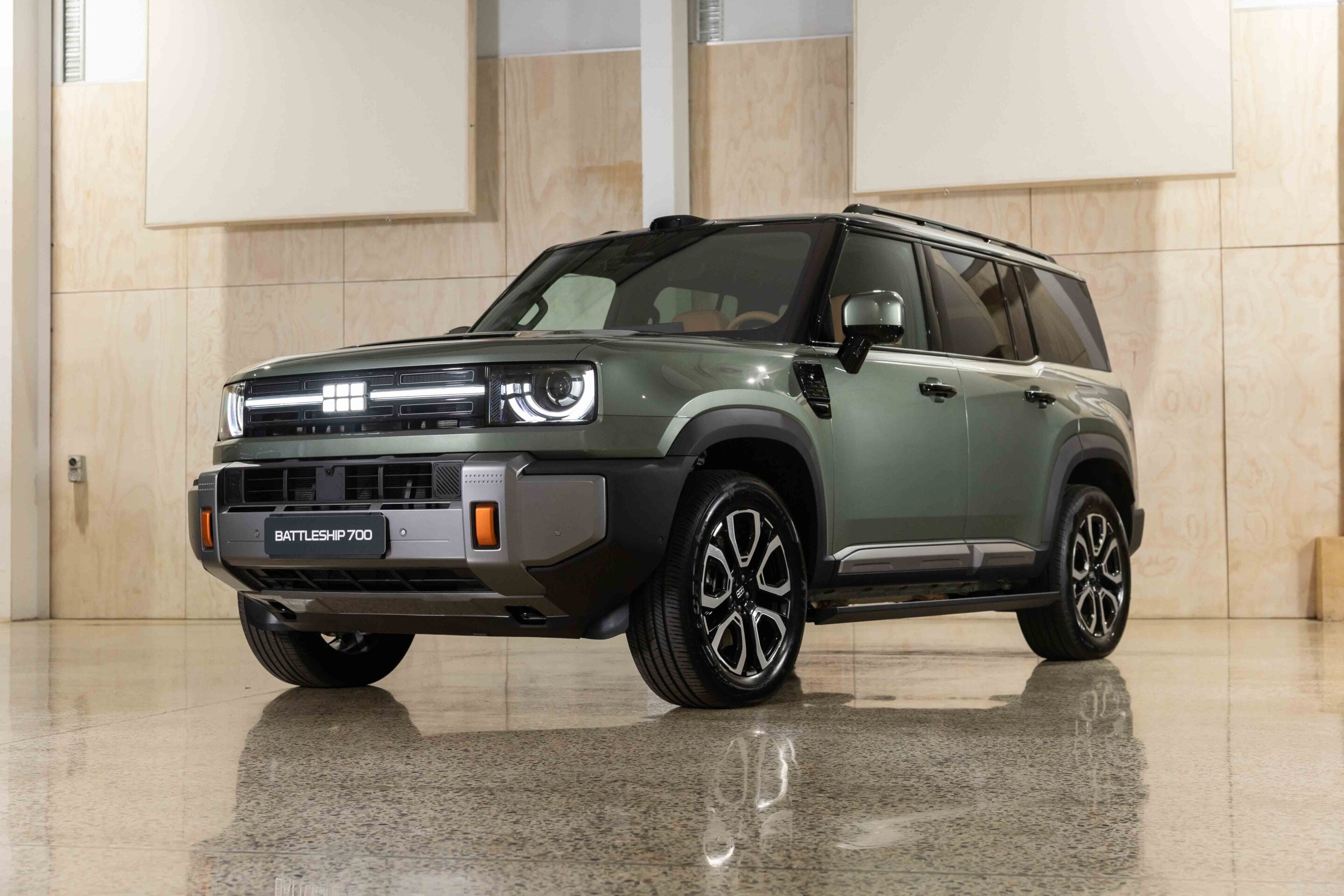 Front three-quarter view of a green Land Rover Defender Battleship 700 in a bright showroom.